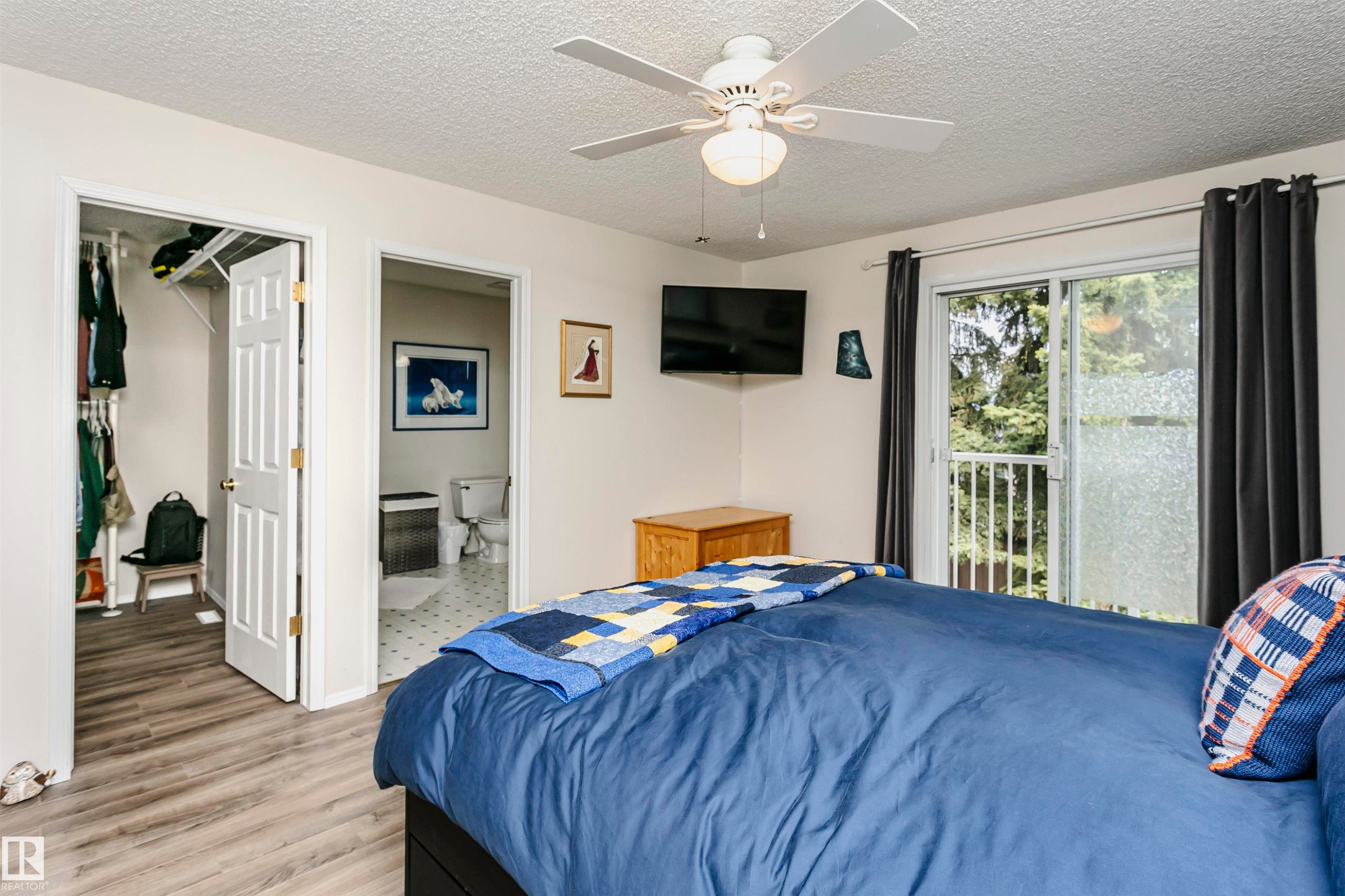 Wood-finish flooring, ceiling fan, white paneled doors, sliding glass door to exterior, and wall-mounted television - #42 9630 176 St Nw, Edmonton, AB - Indoor Photo Showing Bedroom
