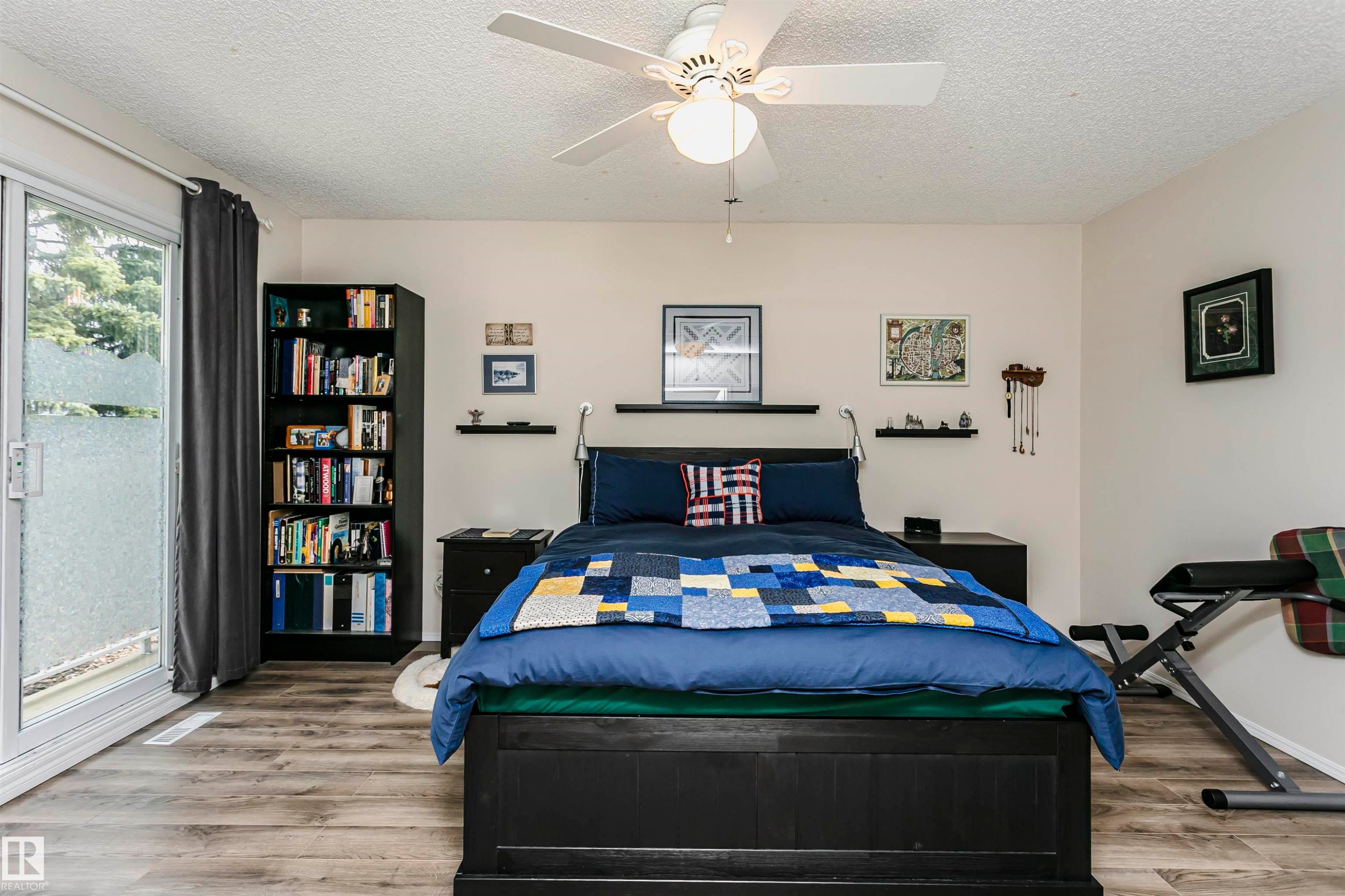 Slider door offering exterior access, wood-finish flooring, ceiling fan with integrated lighting, built-in shelving, and floating wall shelves - #42 9630 176 St Nw, Edmonton, AB - Indoor Photo Showing Bedroom