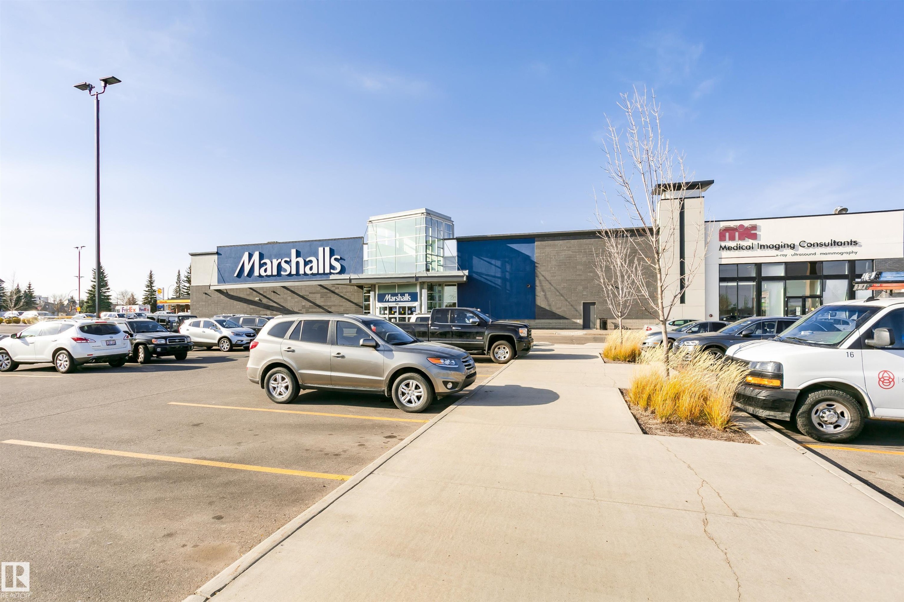 Retail storefront featuring a prominent Marshalls sign, an additional medical imaging consultant office, a large paved parking lot, and a concrete walkway with planted grass - #42 9630 176 St Nw, Edmonton, AB - Outdoor