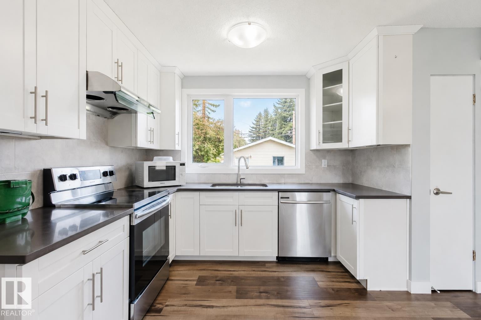 White shaker cabinetry, stainless steel appliances, dark countertops, wood-finish flooring, and a tiled backsplash - 11420 46 Avenue Nw, Edmonton, AB - Indoor Photo Showing Kitchen