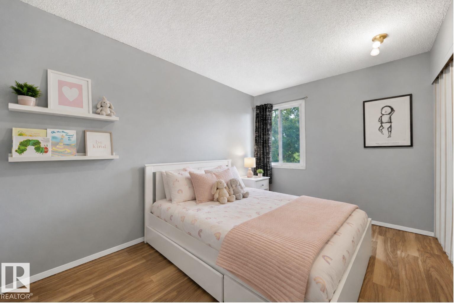 Serene secondary bedroom featuring soft gray walls, white built-in cabinetry with open shelving, wood-finish flooring, recessed ceiling lighting, and a large window with blackout drapery - #44 1415 62 St Nw, Edmonton, AB - Indoor Photo Showing Bedroom