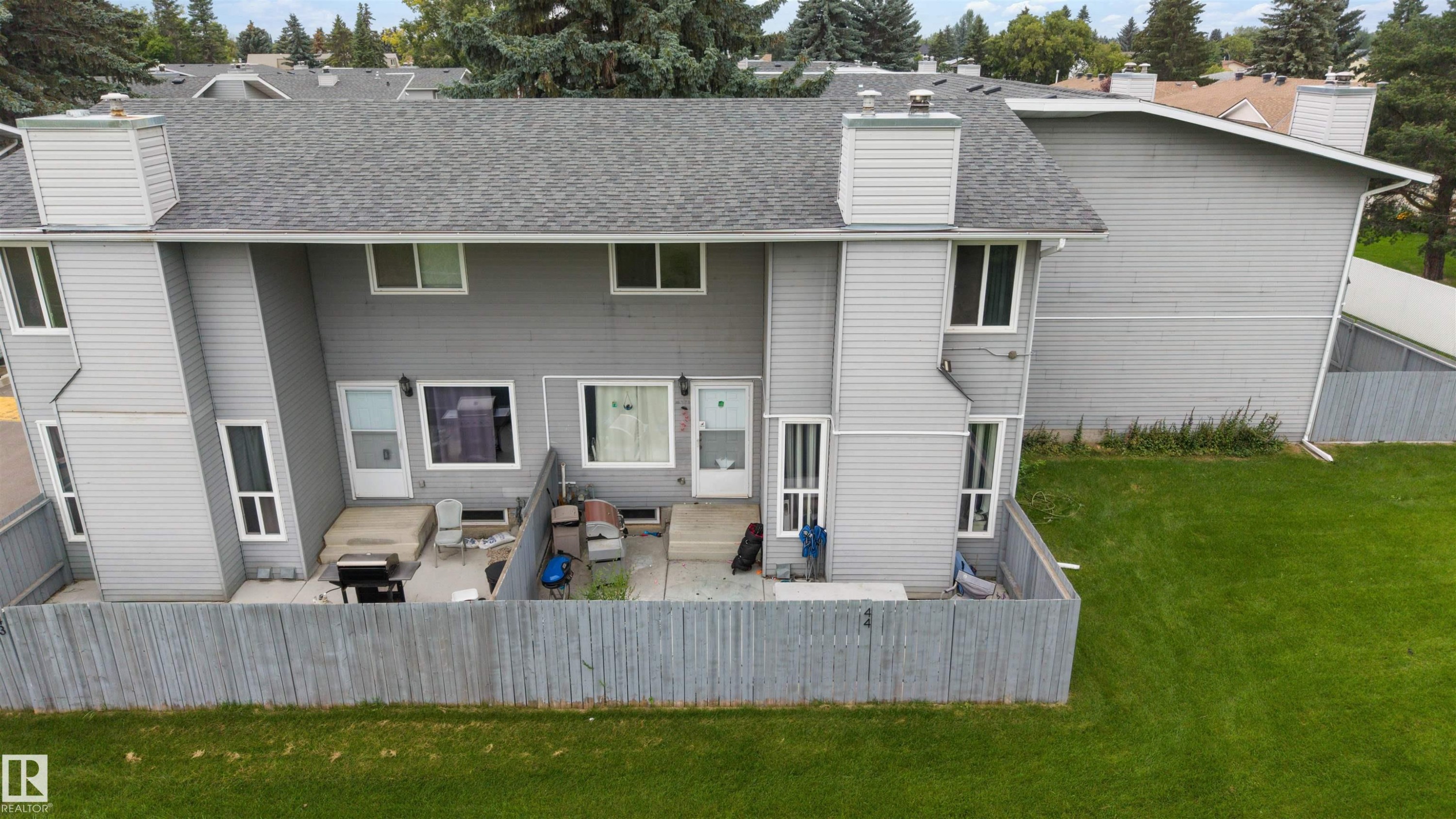 Rear townhouse exterior featuring a private fenced patio, grey horizontal siding, and a gabled roofline with a chimney - #44 1415 62 St Nw, Edmonton, AB - Outdoor With Exterior