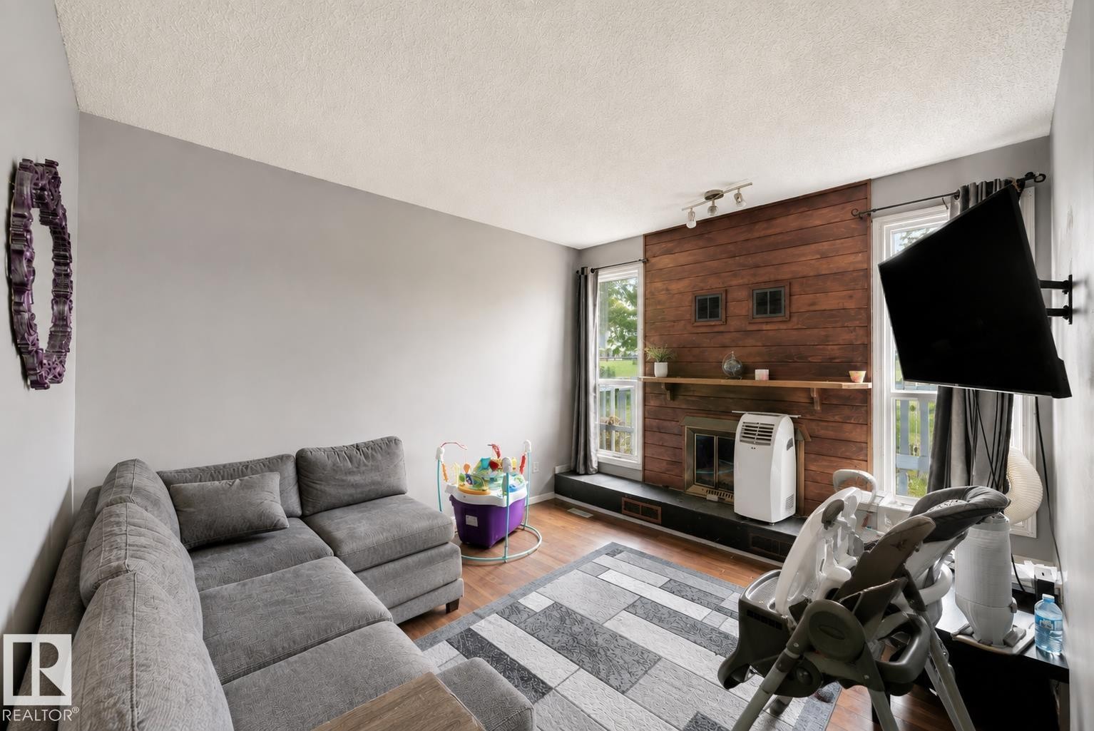 Wood-finish flooring, accent wall with horizontal wood paneling, fireplace with hearth, and natural light from multiple windows - #44 1415 62 St Nw, Edmonton, AB - Indoor Photo Showing Living Room With Fireplace