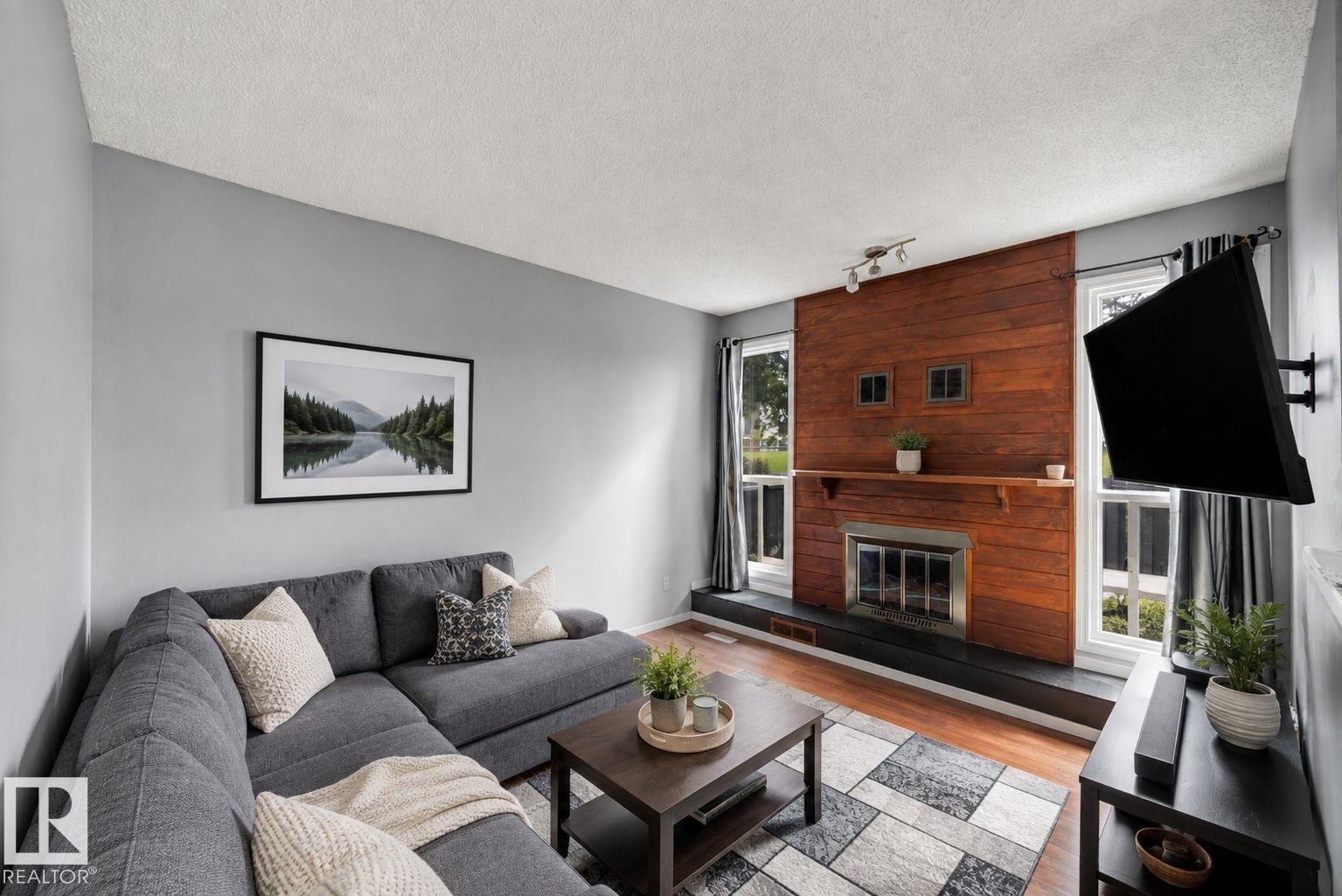 Living room featuring a wood-panel accent wall, built-in fireplace, and wood-finish flooring - #44 1415 62 St Nw, Edmonton, AB - Indoor Photo Showing Living Room With Fireplace
