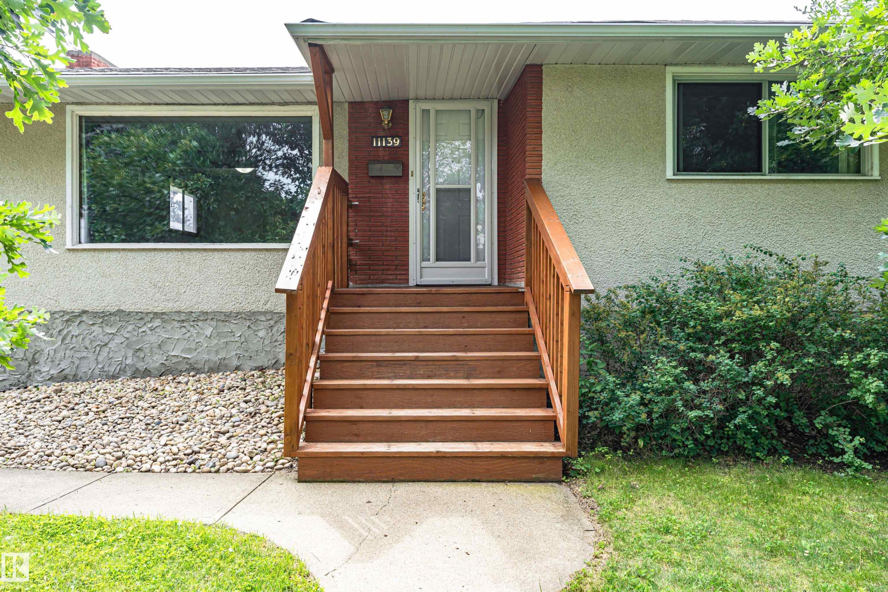 Wood-tone entry stairs with a simple railing, stucco exterior, and brick-clad accent wall - 11139 62 Avenue Nw, Edmonton, AB - Outdoor With Exterior