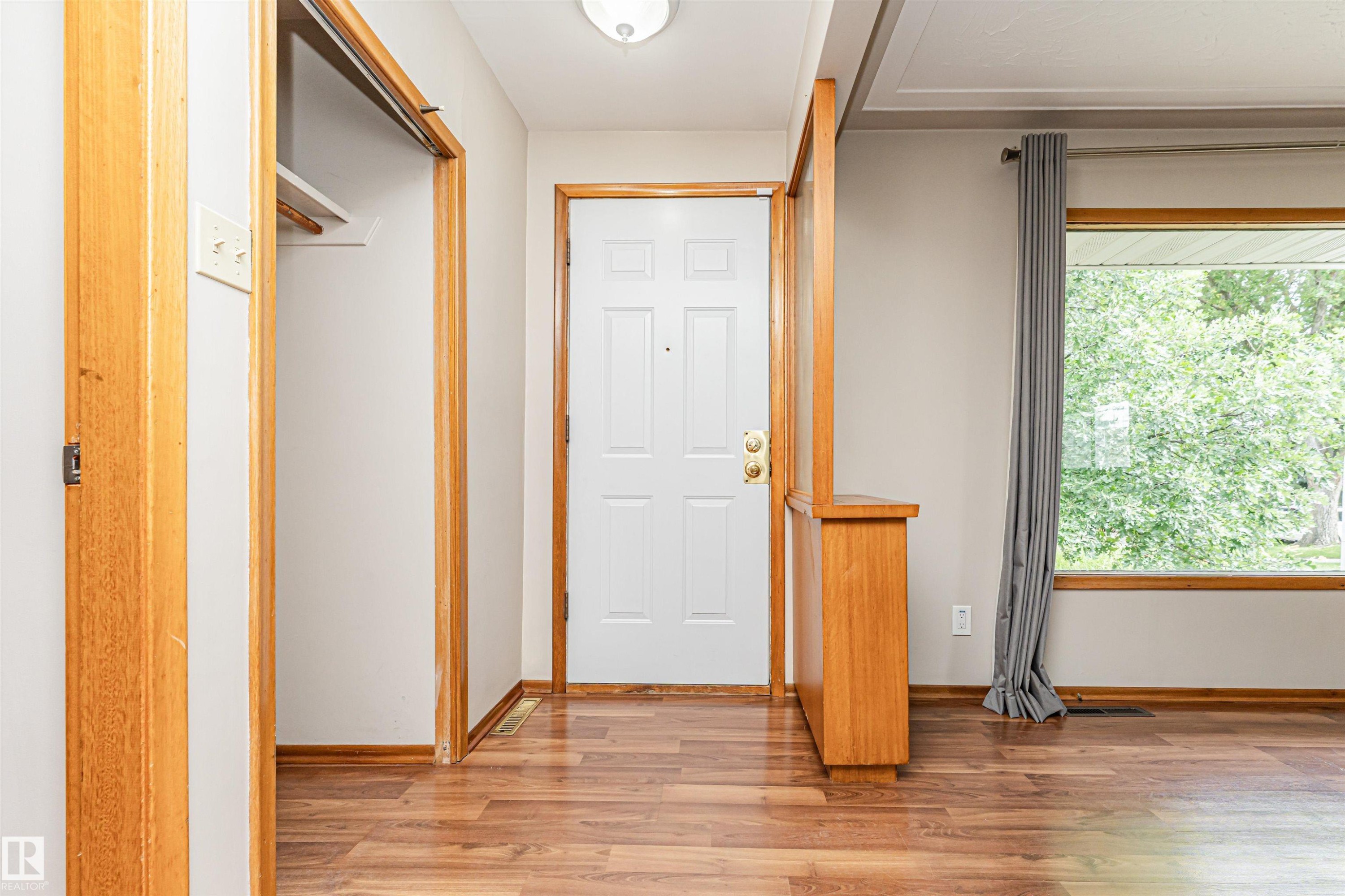 Wood-finish flooring, white paneled entry door, built-in wooden half-wall, wood trim, and a large window - 11139 62 Avenue Nw, Edmonton, AB - Indoor Photo Showing Other Room