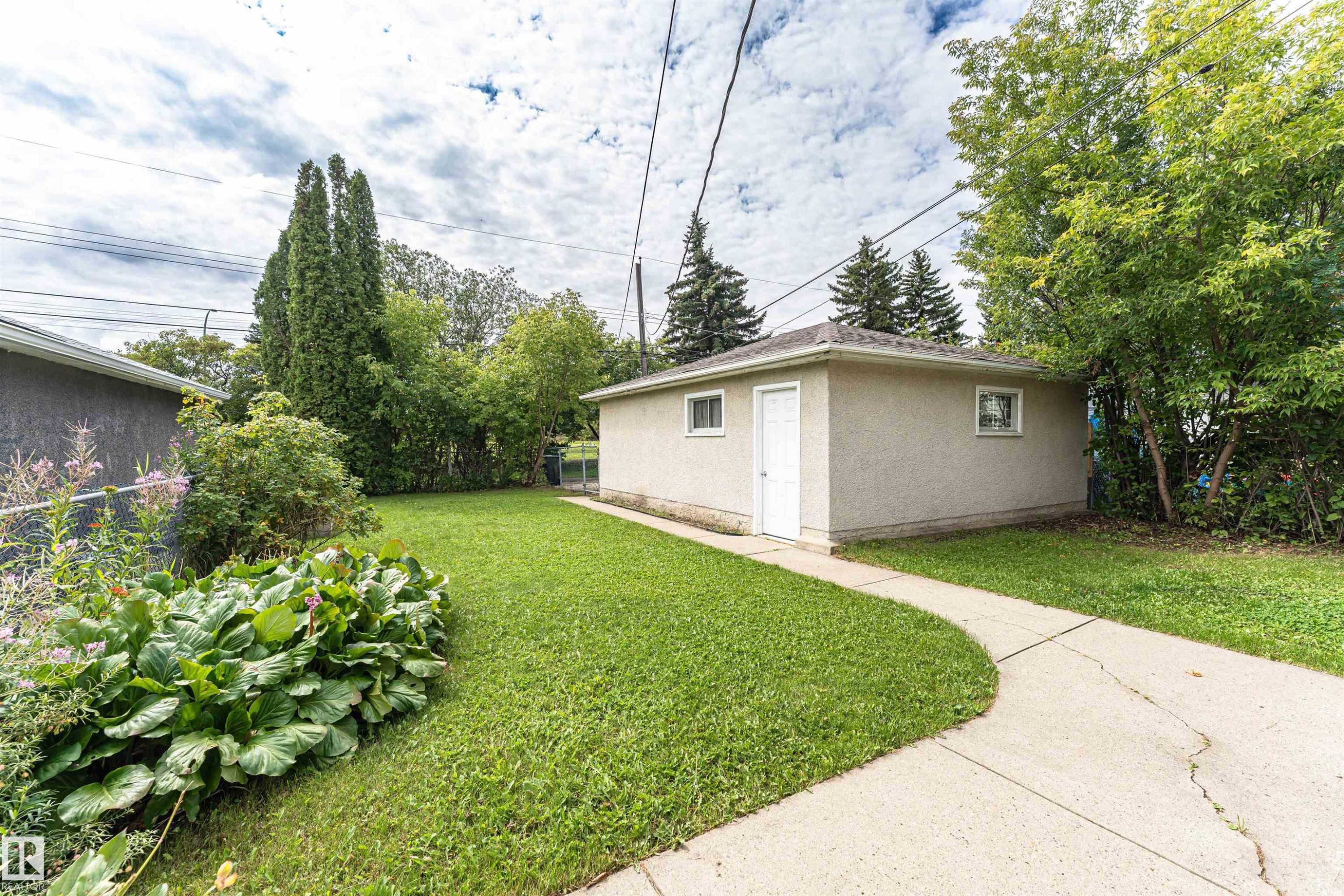 Detached garage with stucco exterior, concrete pathway, and surrounding green lawn - 11139 62 Avenue Nw, Edmonton, AB - Outdoor