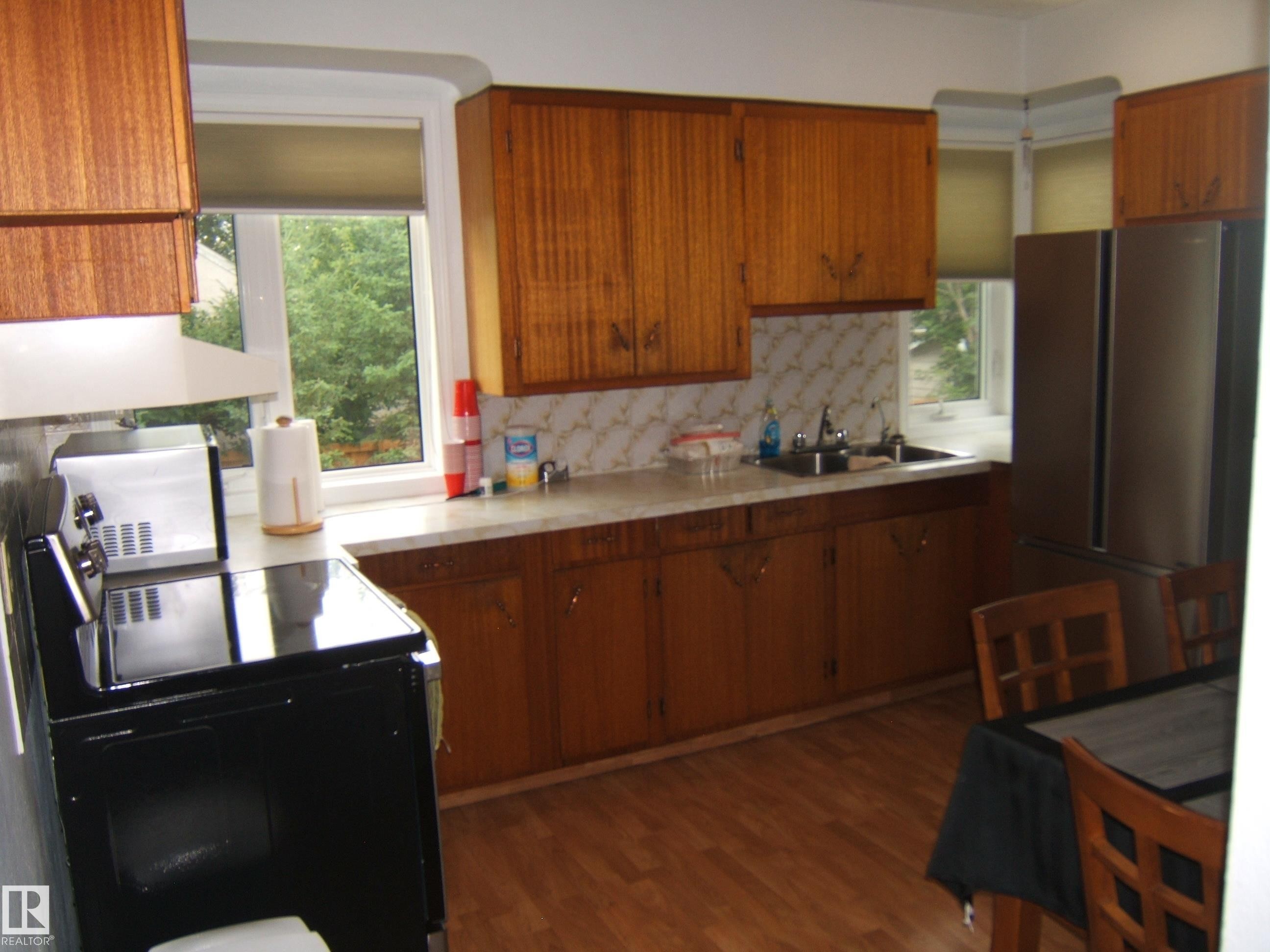 Wood-finish flooring, wood cabinetry, built-in stainless steel refrigerator, white countertops, and a double basin stainless steel sink - 4809 47A Street, Two Hills, AB - Indoor Photo Showing Kitchen