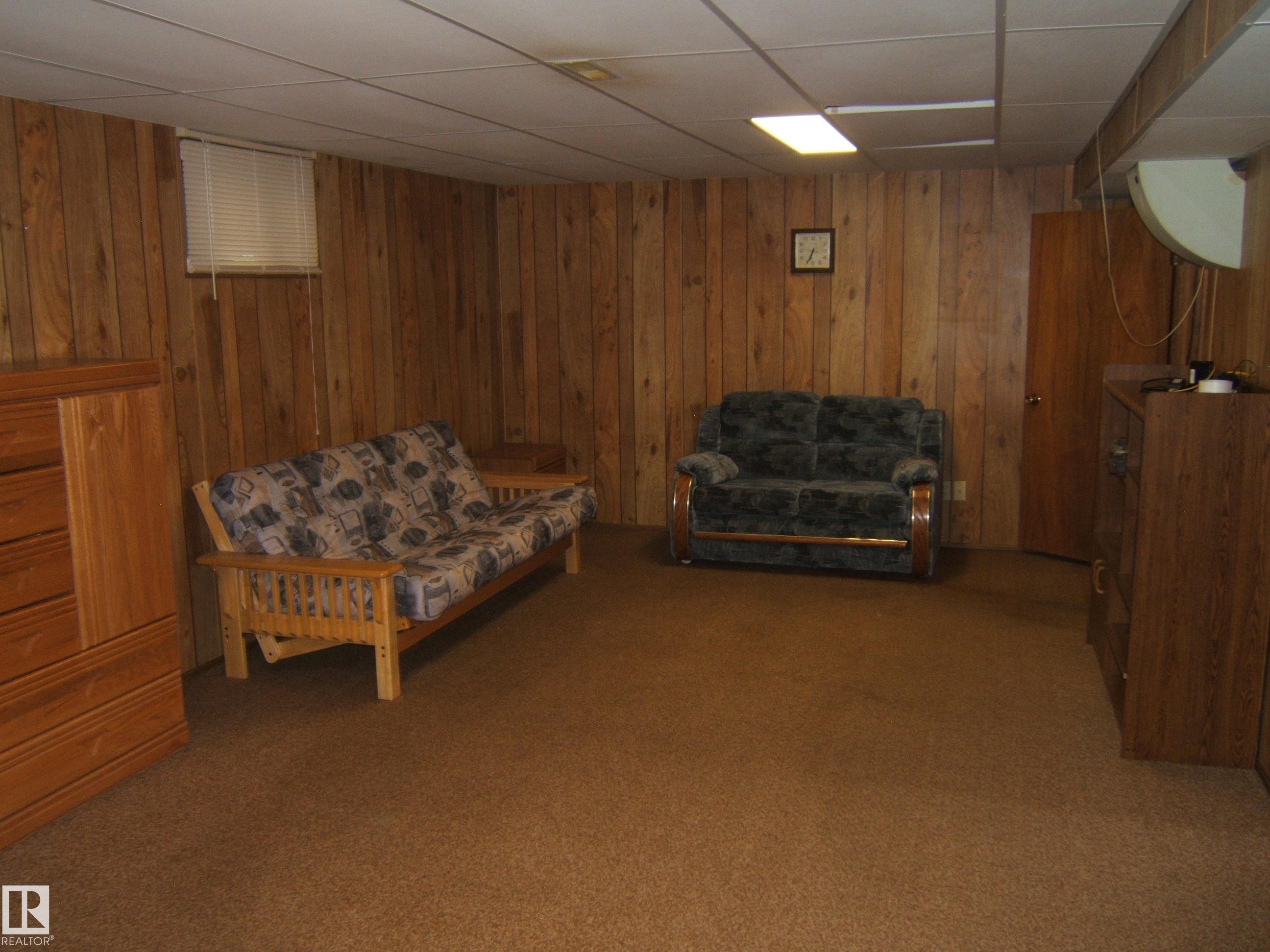 Finished basement recreation room featuring warm wood-paneled walls, cork flooring, recessed ceiling lighting, and multiple seating areas ideal for leisure and entertainment - 4809 47A Street, Two Hills, AB - Indoor