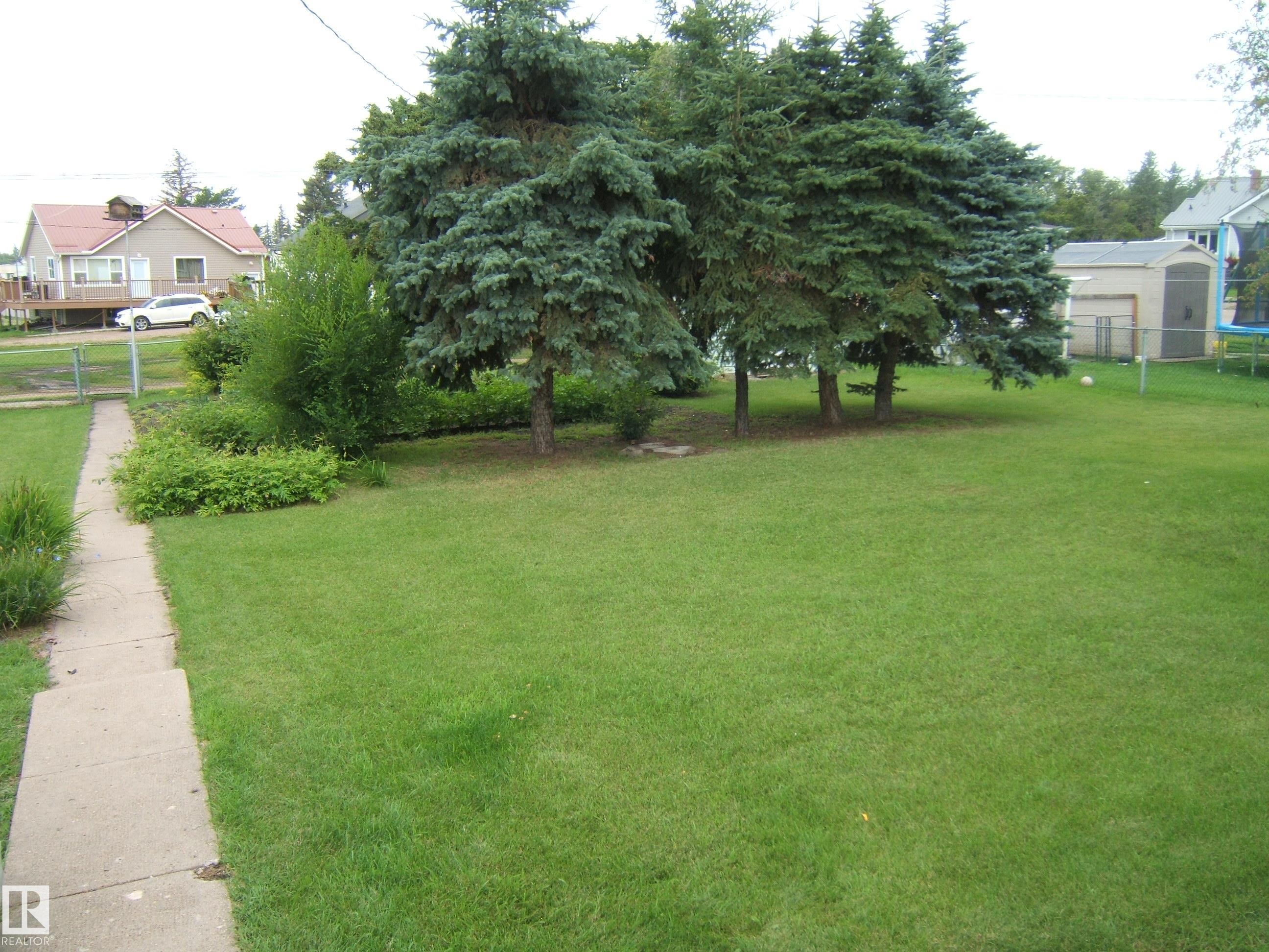 Expansive manicured lawn with mature shade trees and established landscaping - 4809 47A Street, Two Hills, AB - Outdoor