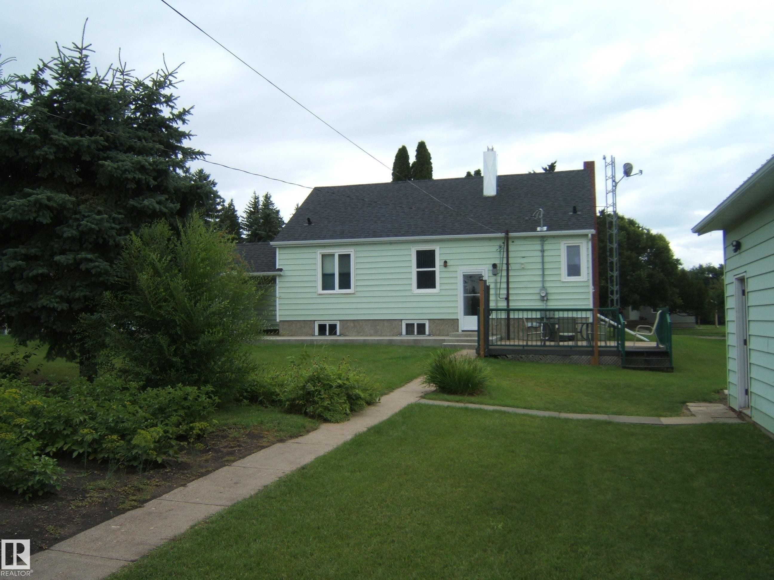 Charming elevated home featuring light green horizontal siding, a dark pitched roof, and a covered front porch with deck access - 4809 47A Street, Two Hills, AB - Outdoor