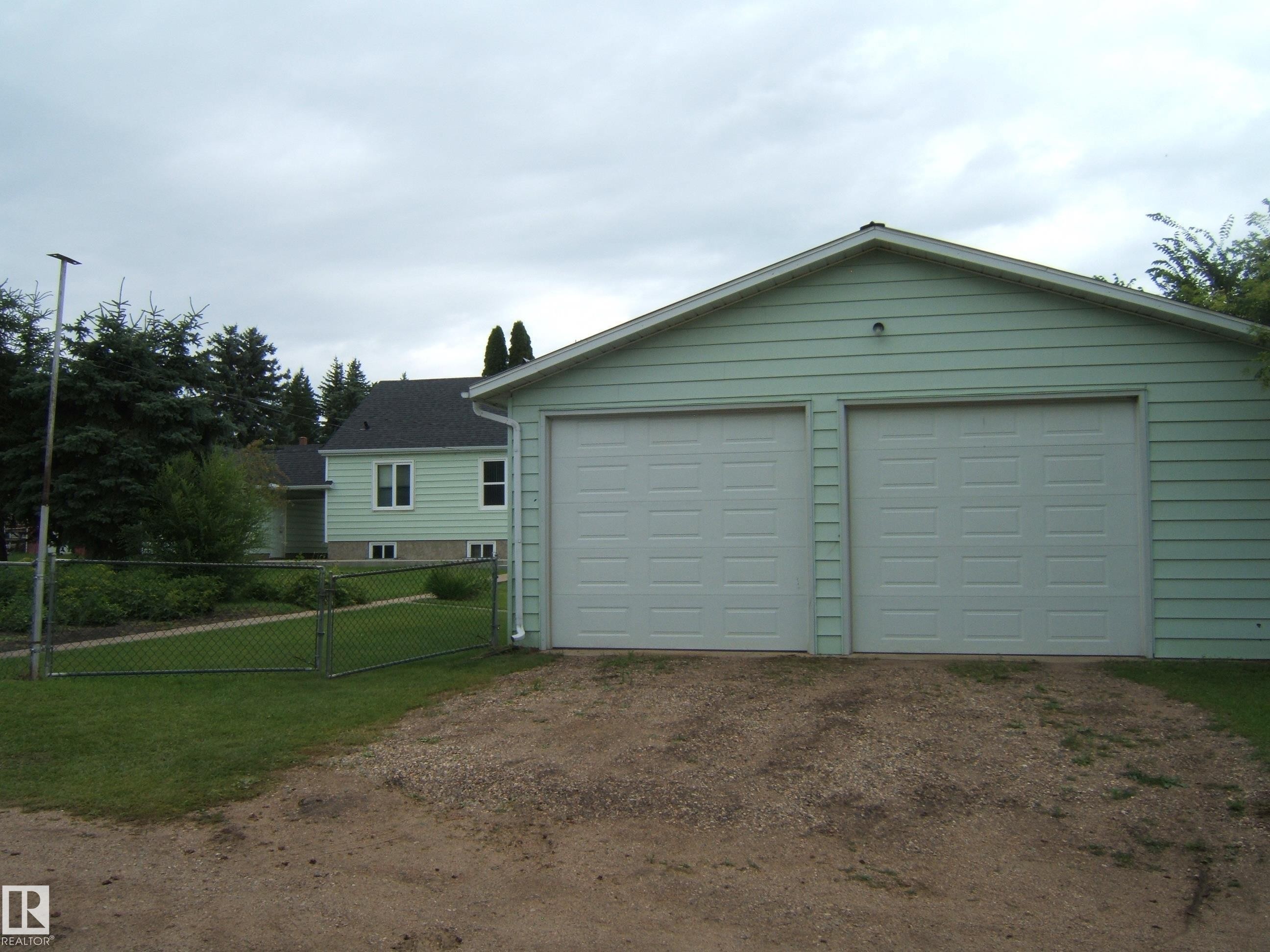 Spacious two-car garage with dual overhead doors and light-colored siding - 4809 47A Street, Two Hills, AB - Outdoor
