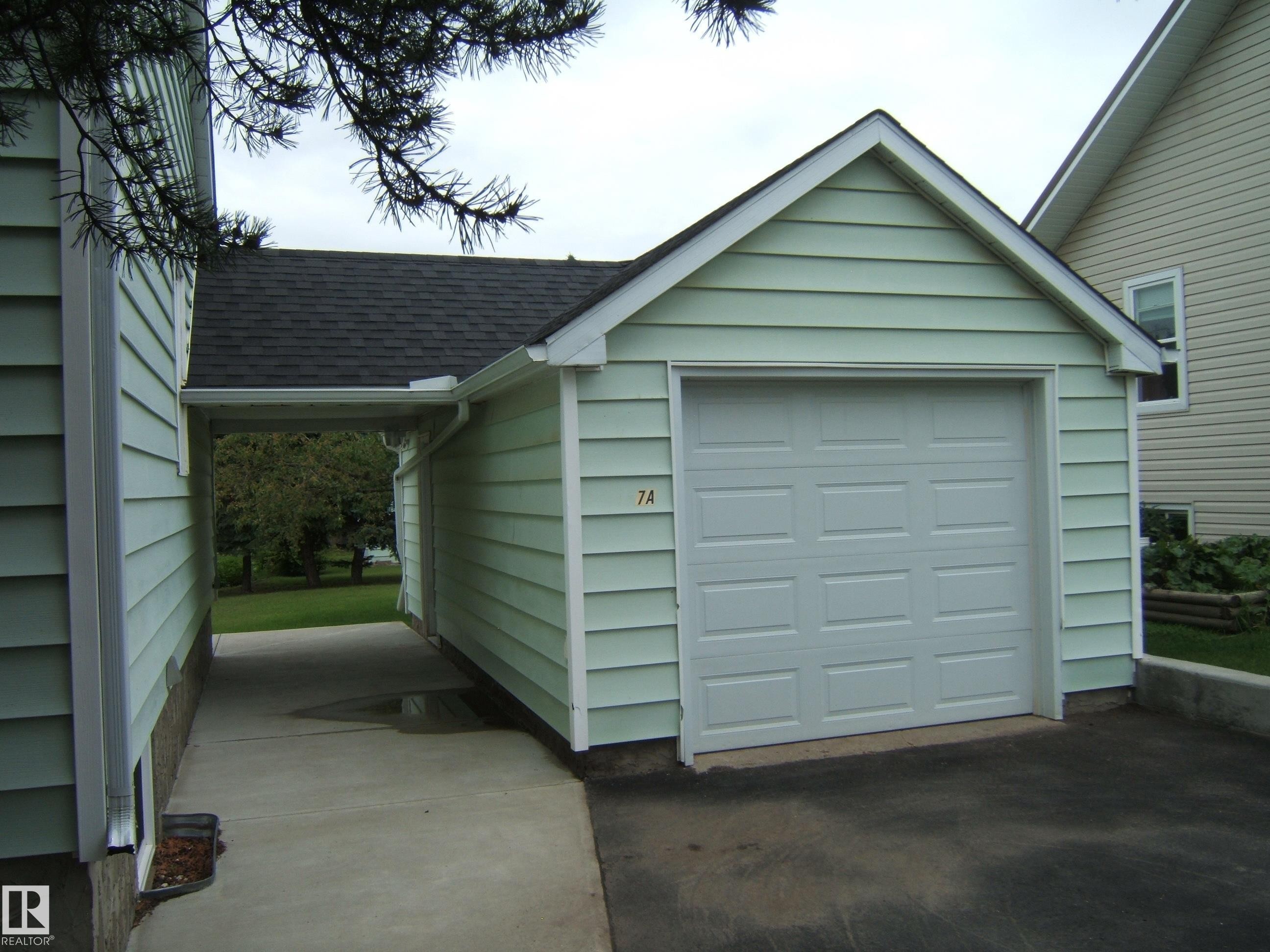 Detached garage with horizontal siding, a paneled garage door, and a covered breezeway - 4809 47A Street, Two Hills, AB - Outdoor With Exterior