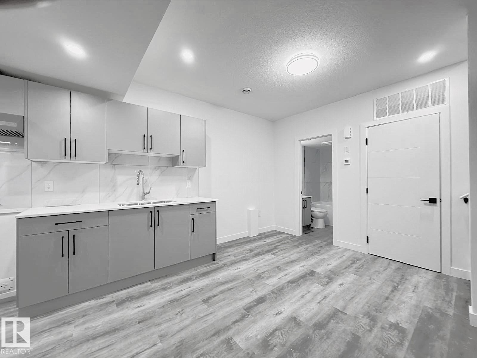 Contemporary kitchen featuring shaker-style cabinetry, quartz countertops, a double basin sink, and a tiled backsplash - 1312 35 Street Nw, Edmonton, AB