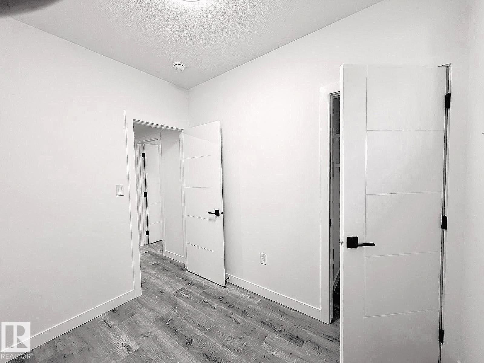 Wood-finish flooring with white baseboards, recessed ceiling lighting, and modern white doors with black hardware - 1312 35 Street Nw, Edmonton, AB