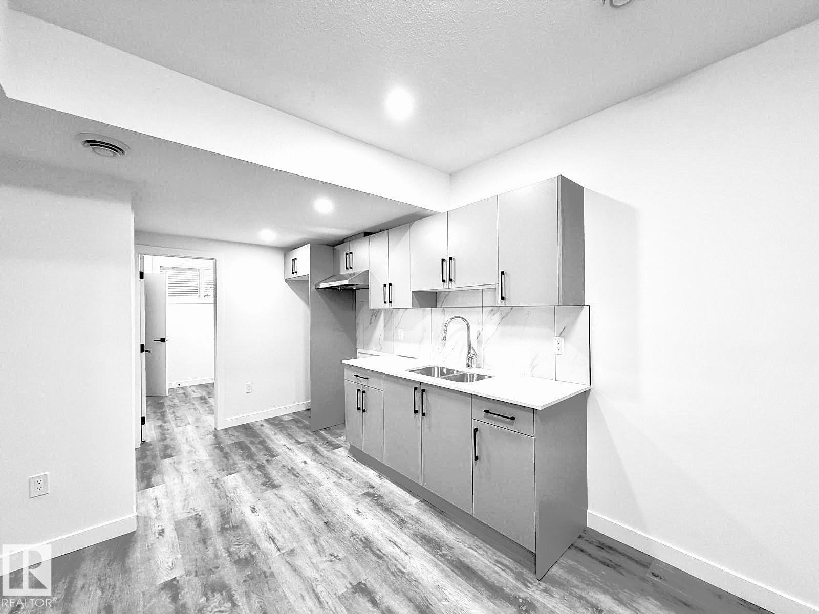 Kitchenette featuring light gray cabinetry, a dual-basin stainless steel sink, a tile backsplash, and wood-finish flooring - 1312 35 Street Nw, Edmonton, AB