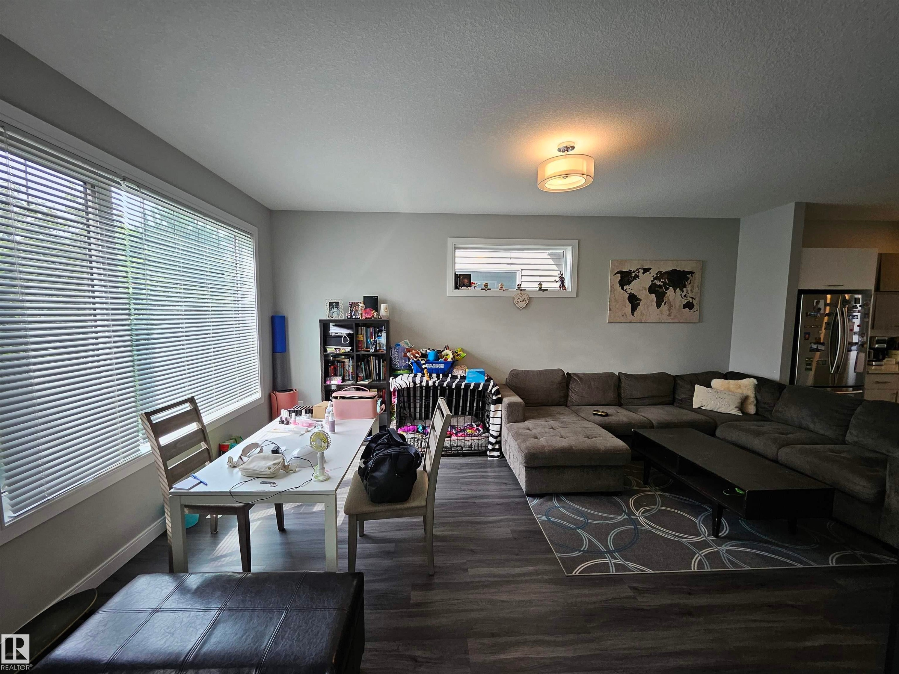 Spacious living area featuring wood-finish flooring, a large window with horizontal blinds, neutral wall tones, and a flush-mount ceiling light fixture - 15212 98 Avenue Nw, Edmonton, AB - Indoor Photo Showing Living Room