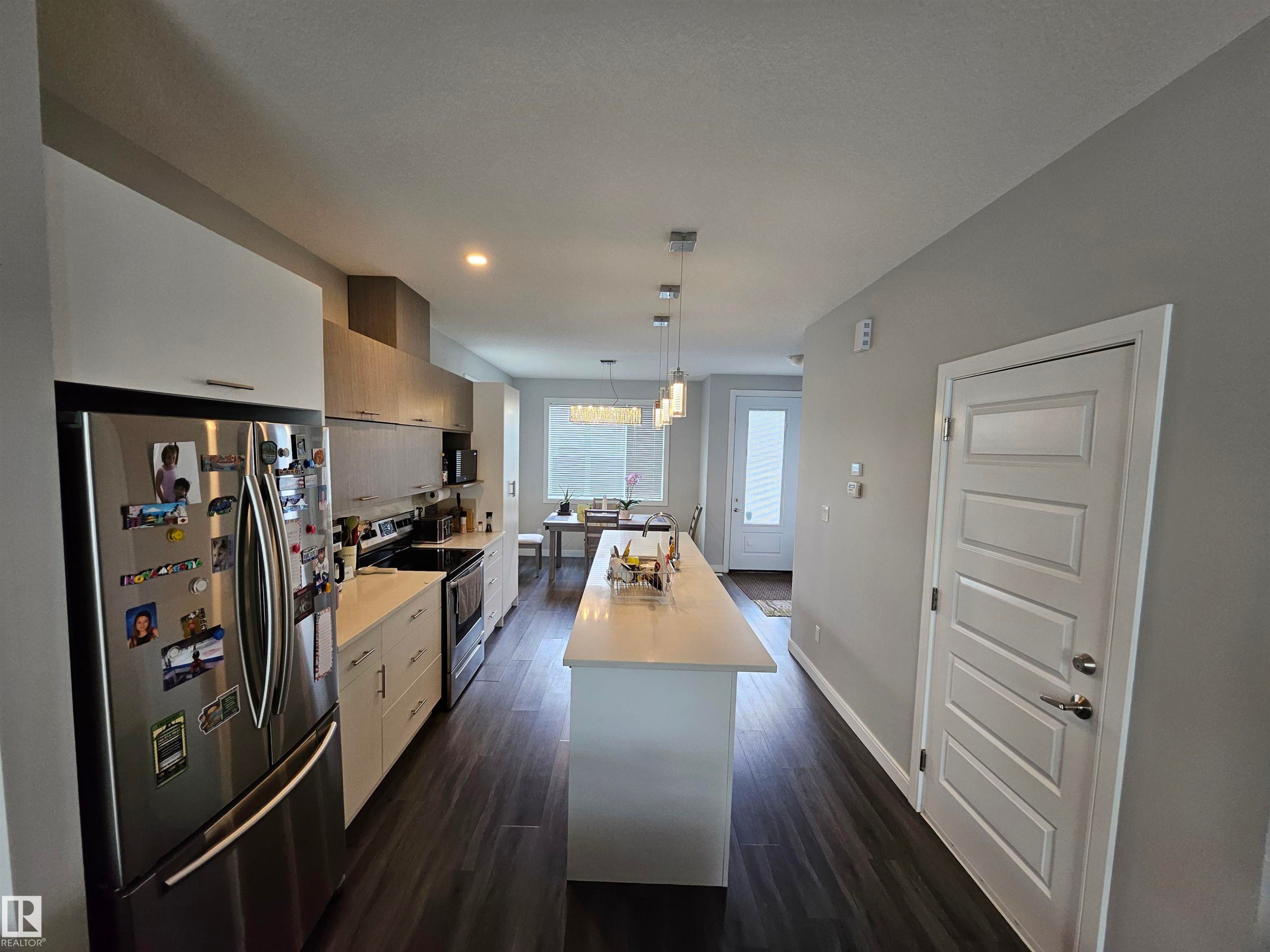 Expansive kitchen with a large central island, wood-finish flooring, white cabinetry, stainless steel appliances, and a dining area with a chandelier - 15212 98 Avenue Nw, Edmonton, AB - Indoor Photo Showing Other Room