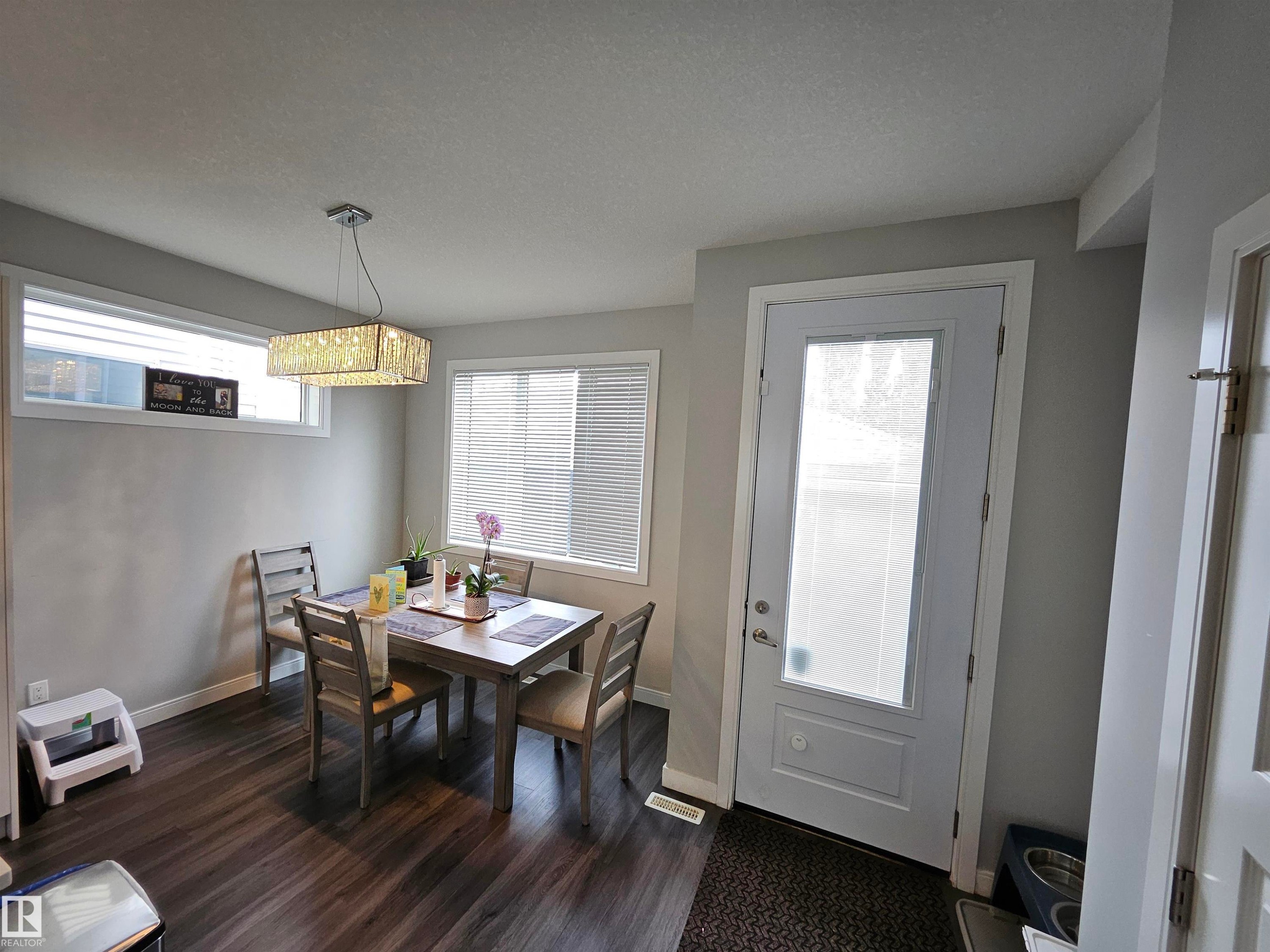 Wood-finish flooring, recessed window, large window with blinds, frosted glass panel door, and a crystal chandelier - 15212 98 Avenue Nw, Edmonton, AB - Indoor Photo Showing Dining Room