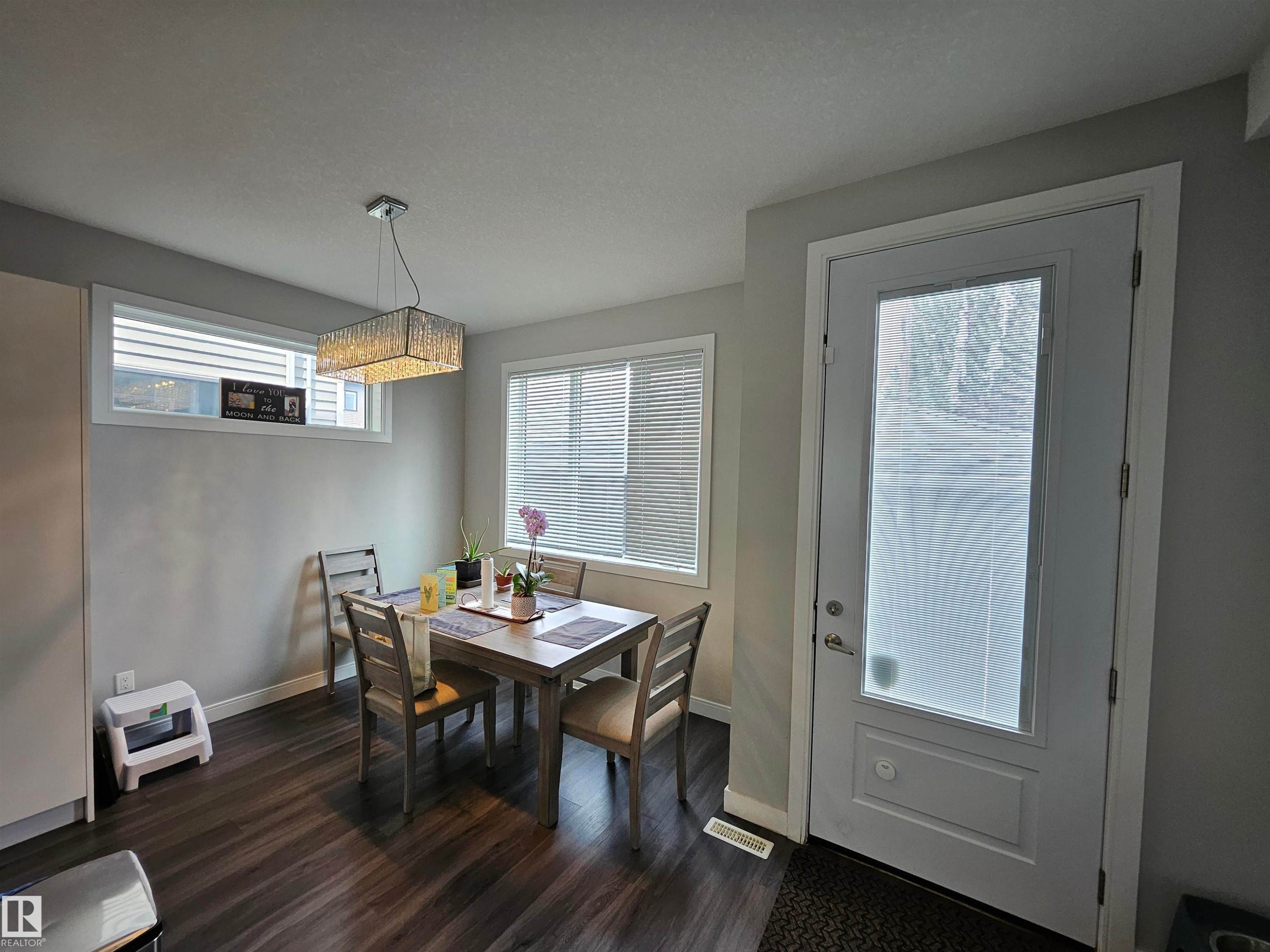 Wood-finish flooring, white trim, rectangular crystal chandelier, transom window, and a paneled entry door with frosted glass - 15212 98 Avenue Nw, Edmonton, AB - Indoor Photo Showing Dining Room