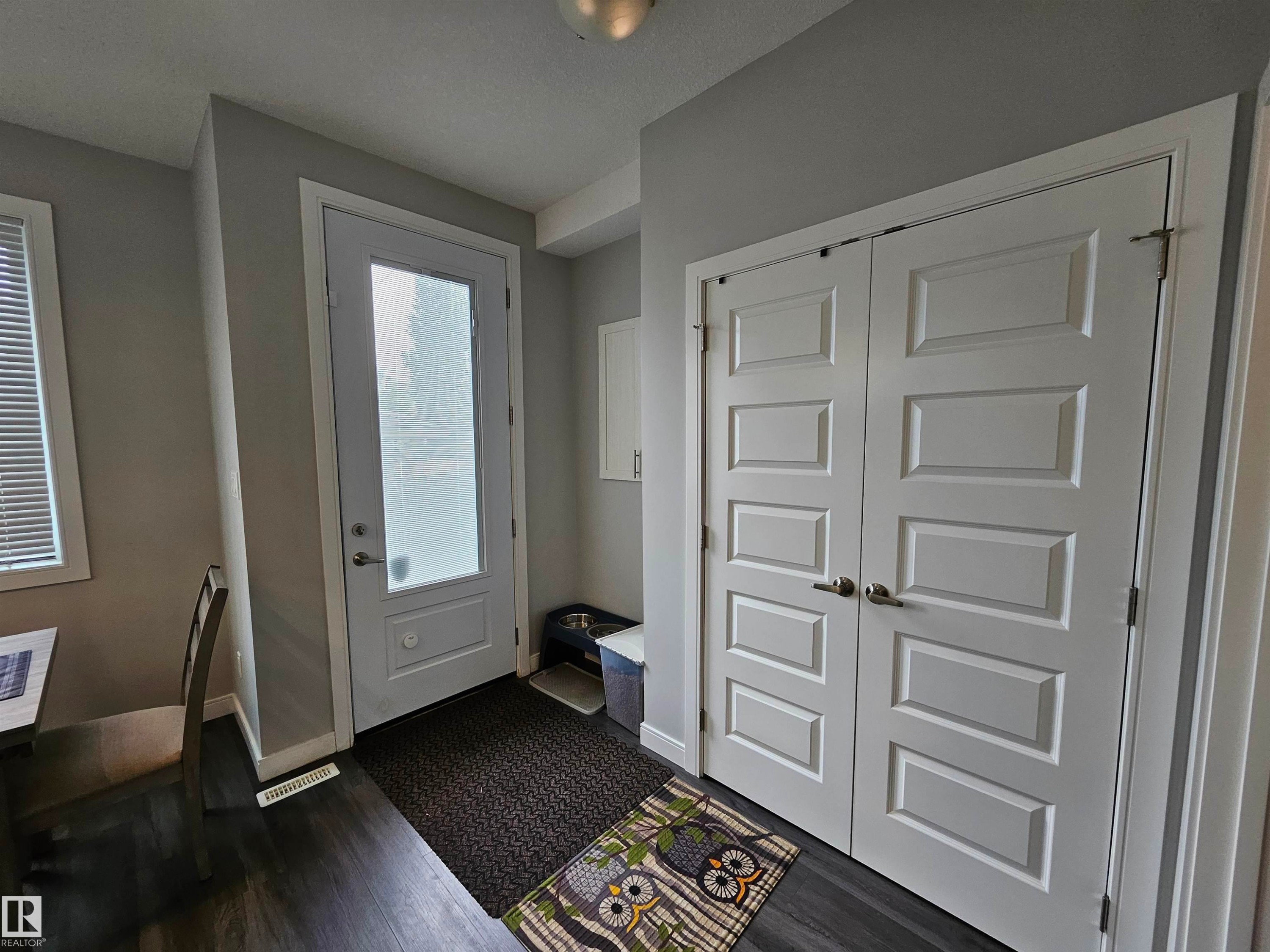 Entryway featuring wood-finish flooring, a full-lite exterior door with privacy glass, white trim, and bi-fold closet doors with paneling - 15212 98 Avenue Nw, Edmonton, AB - Indoor Photo Showing Other Room
