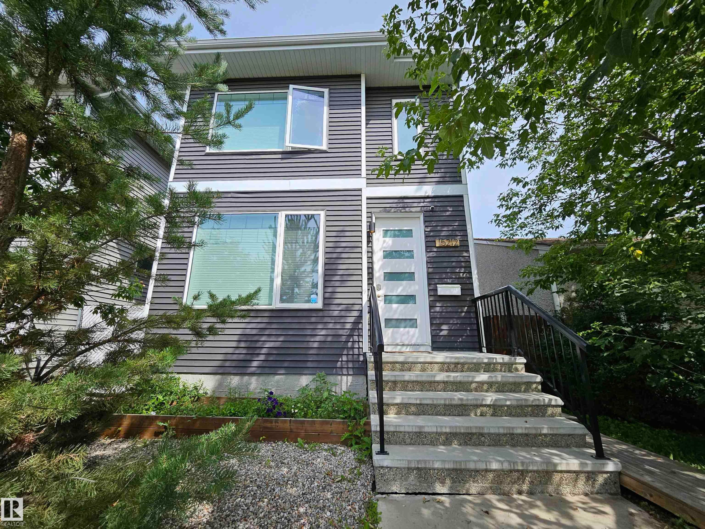 Modern facade with dark horizontal siding, white trim, and a prominent white entry door - 15212 98 Avenue Nw, Edmonton, AB - Outdoor