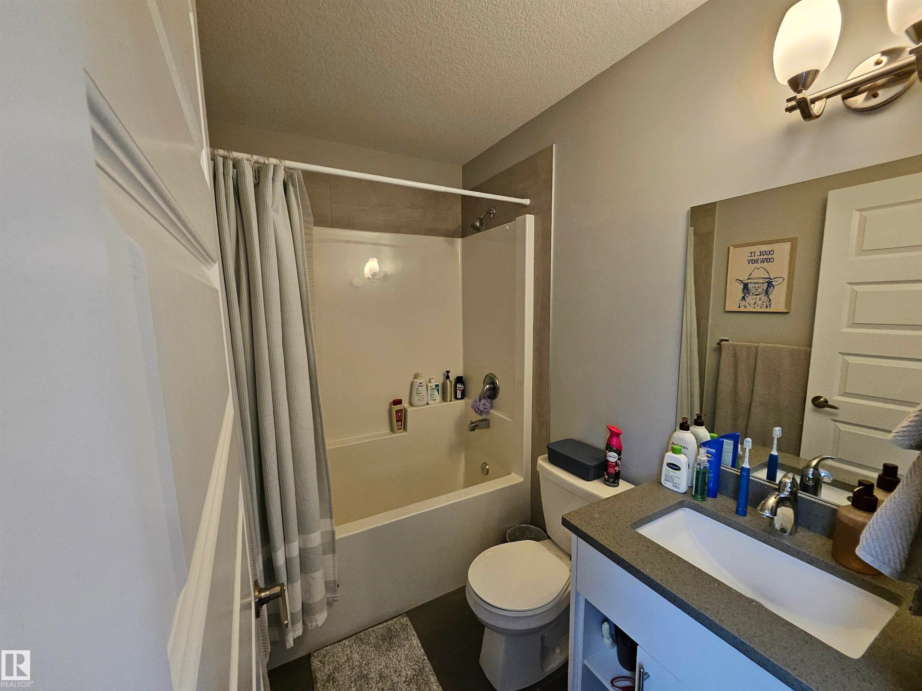 Built-in bathtub with shower, vanity with integrated sink, stone-finish countertop, and wall-mounted lighting fixture - 15212 98 Avenue Nw, Edmonton, AB - Indoor Photo Showing Bathroom