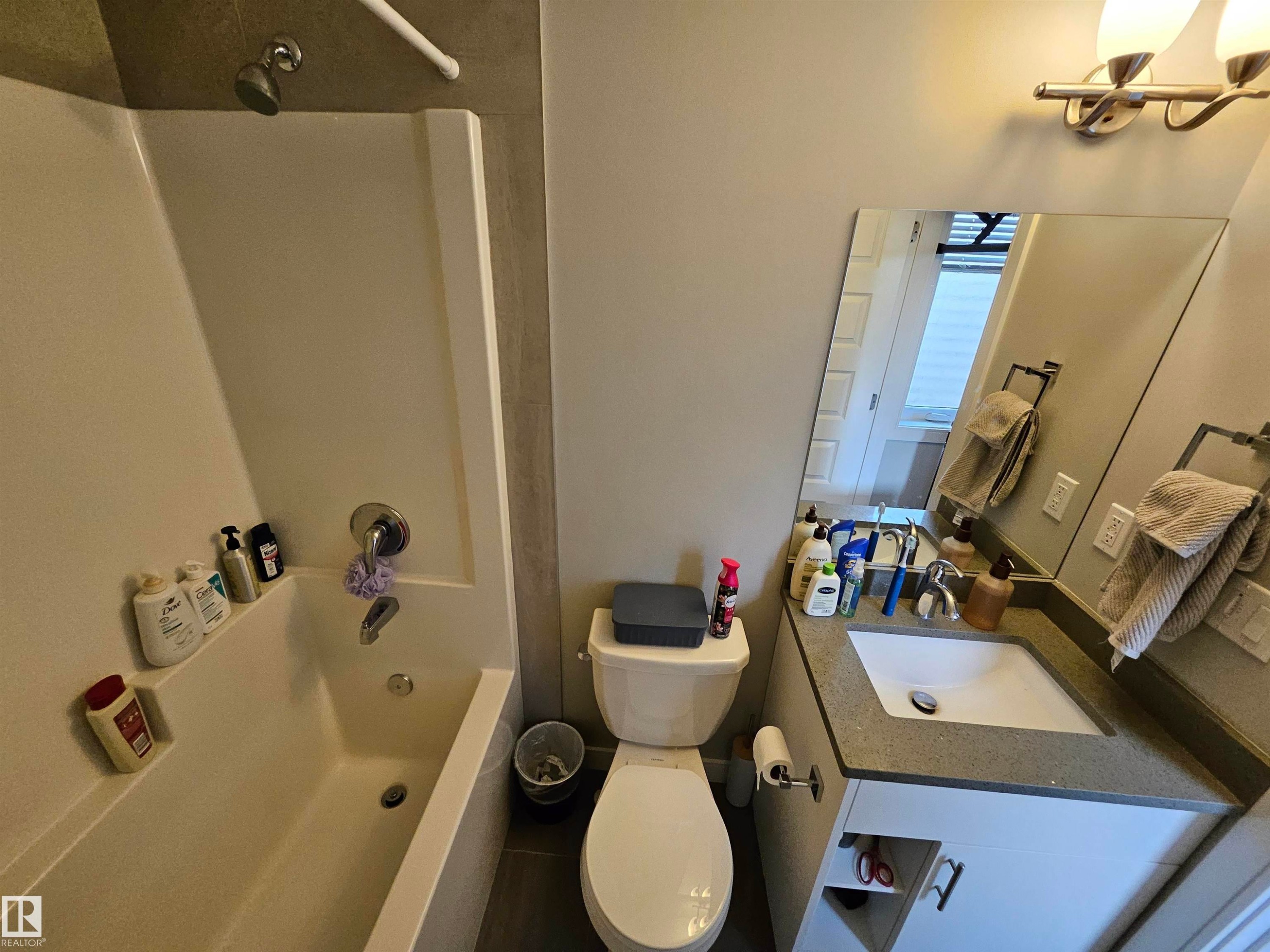 White bathtub and shower combination with chrome fixtures, a vanity with a white basin sink, and a framed mirror - 15212 98 Avenue Nw, Edmonton, AB - Indoor Photo Showing Bathroom