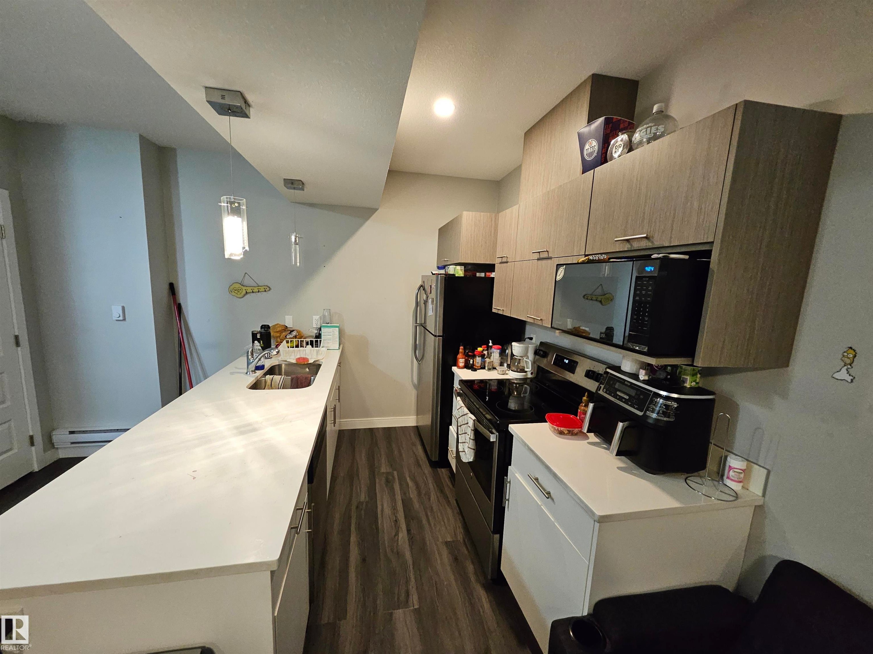 Galley kitchen featuring wood-finish cabinetry with stainless hardware, stainless steel appliances, a white countertop, and pendant lighting - 15212 98 Avenue Nw, Edmonton, AB - Indoor