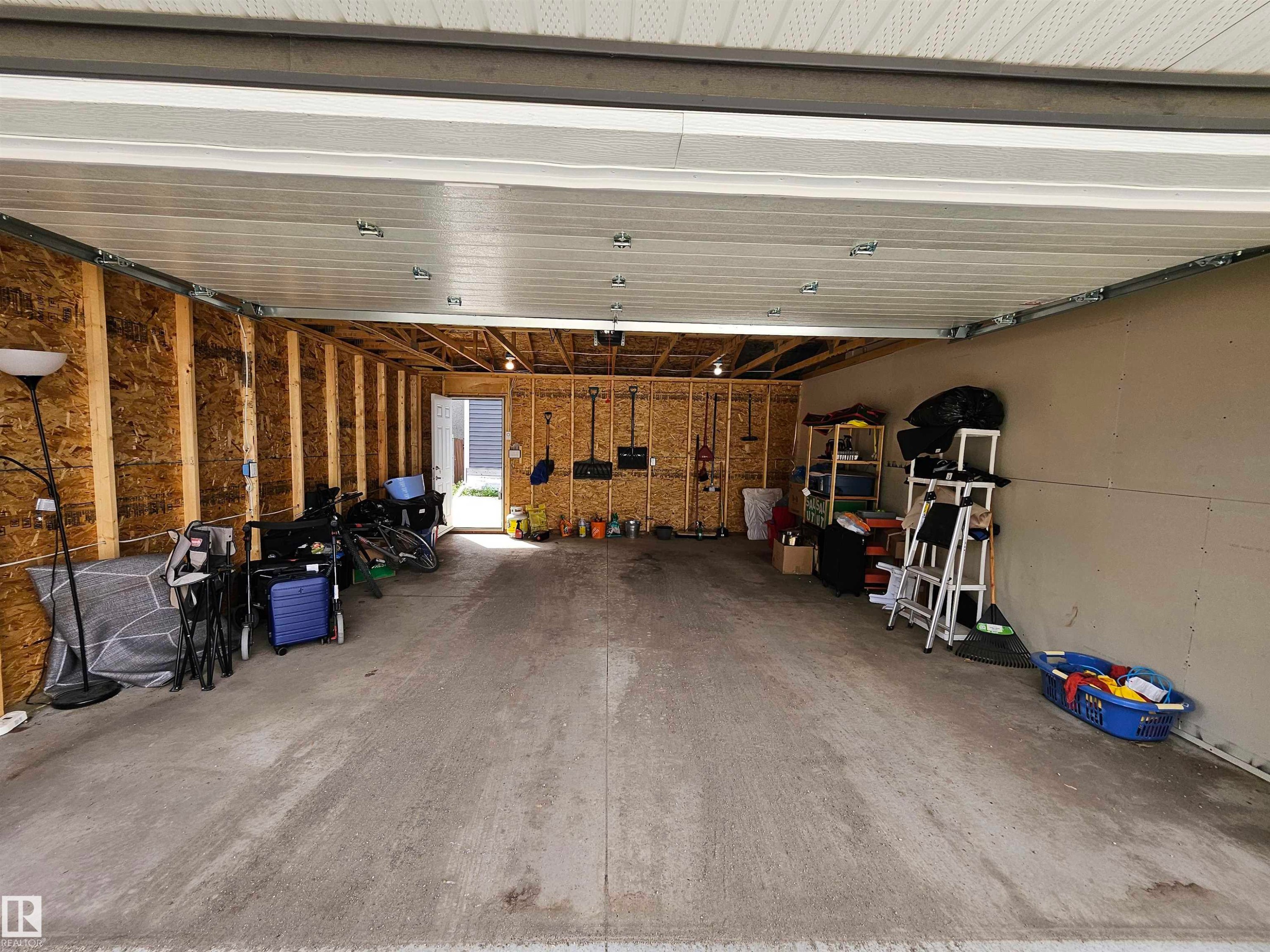 Spacious garage with concrete flooring, exposed wood-frame walls, and a large overhead garage door - 15212 98 Avenue Nw, Edmonton, AB - Indoor Photo Showing Garage