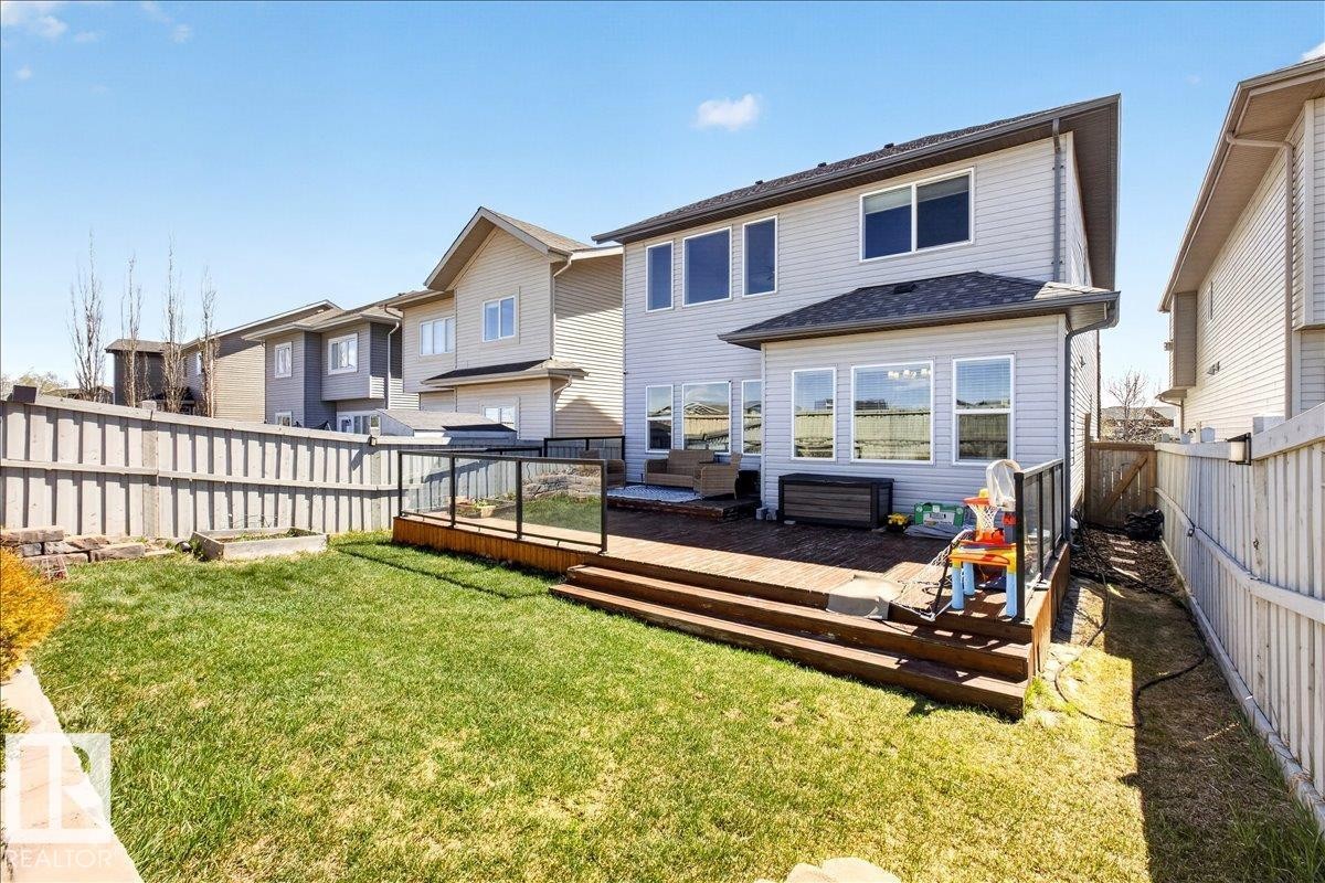 Expansive backyard featuring a manicured lawn, a multi-level wood deck with glass panel railing, and a vinyl-sided exterior with multiple windows - 3936 Claxton Loop Sw, Edmonton, AB - Outdoor With Deck Patio Veranda With Exterior