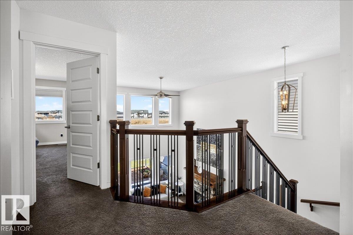 Open upper-level landing with dark wood and wrought iron railing, white paneled doors, and a decorative pendant light fixture - 3936 Claxton Loop Sw, Edmonton, AB - Indoor Photo Showing Other Room