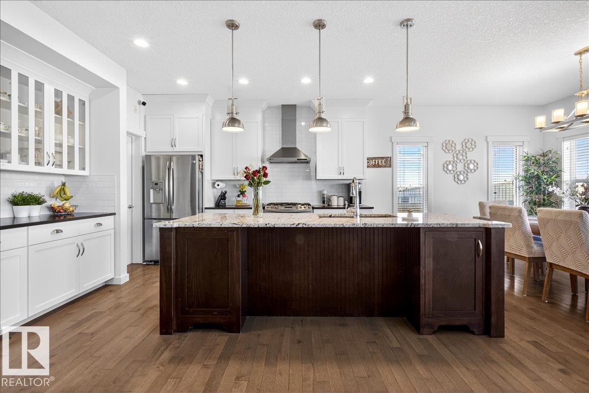 Kitchen featuring wood-finish flooring, a central island with a sink, white cabinetry with glass-front uppers, stainless steel appliances, and recessed lighting - 3936 Claxton Loop Sw, Edmonton, AB - Indoor Photo Showing Kitchen With Upgraded Kitchen