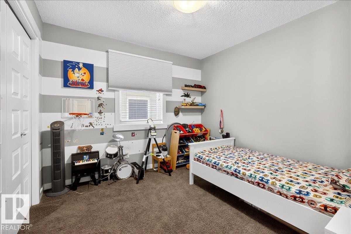 Textured carpeting, smooth painted walls, built-in shelving, white paneled door, and a window with blinds - 3936 Claxton Loop Sw, Edmonton, AB - Indoor Photo Showing Bedroom