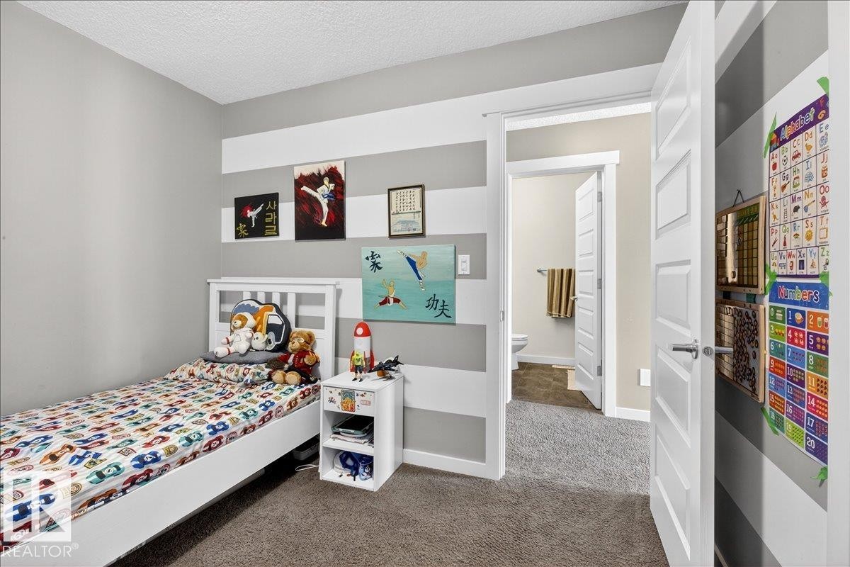 Bright bedroom featuring carpet flooring, built-in wall shelving with display niches, a white wood-finish bed frame, and bedside storage cabinet - 3936 Claxton Loop Sw, Edmonton, AB - Indoor Photo Showing Bedroom