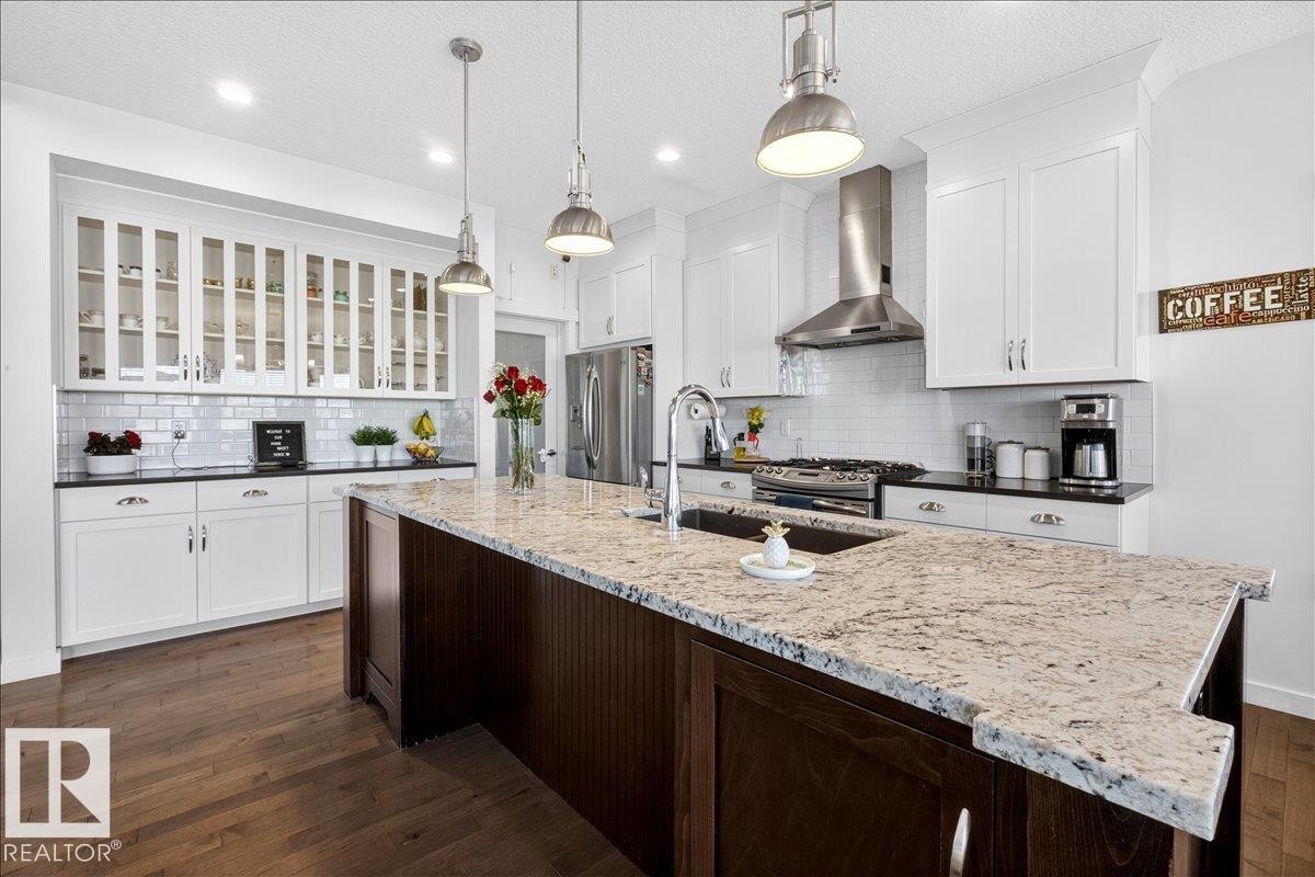 Kitchen featuring a central island with a built-in sink, stainless steel appliances, white cabinetry, and wood-finish flooring - 3936 Claxton Loop Sw, Edmonton, AB - Indoor Photo Showing Kitchen With Upgraded Kitchen