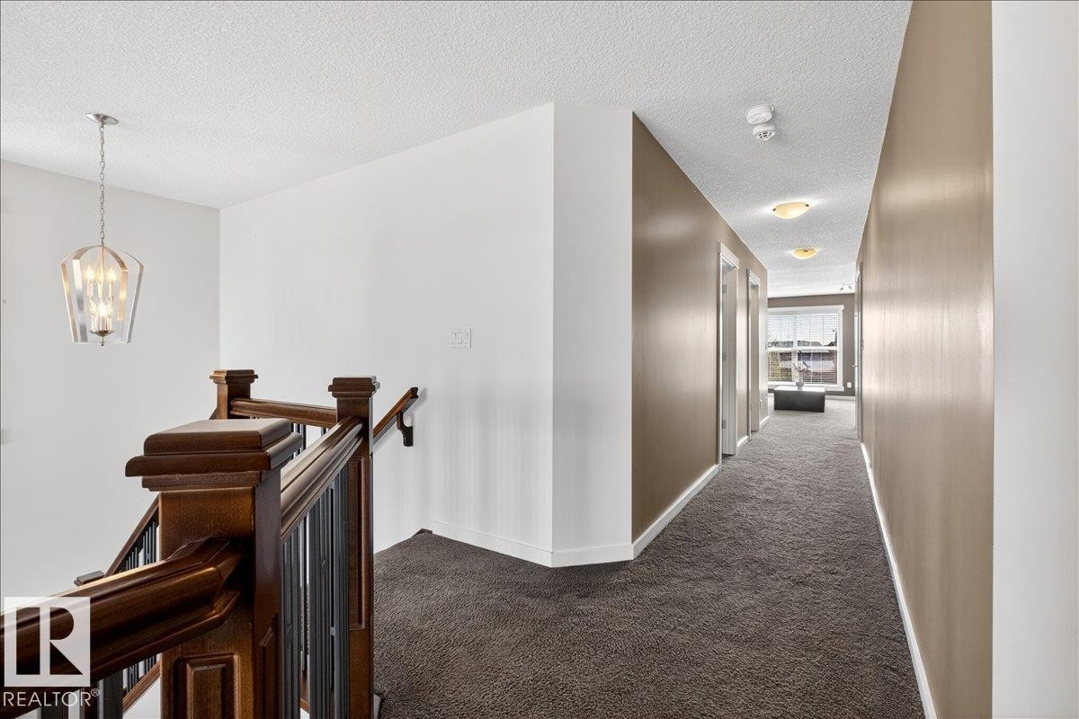Hardwood newel posts with dark balusters, textured carpet flooring, and a modern pendant light fixture - 3936 Claxton Loop Sw, Edmonton, AB - Indoor Photo Showing Other Room