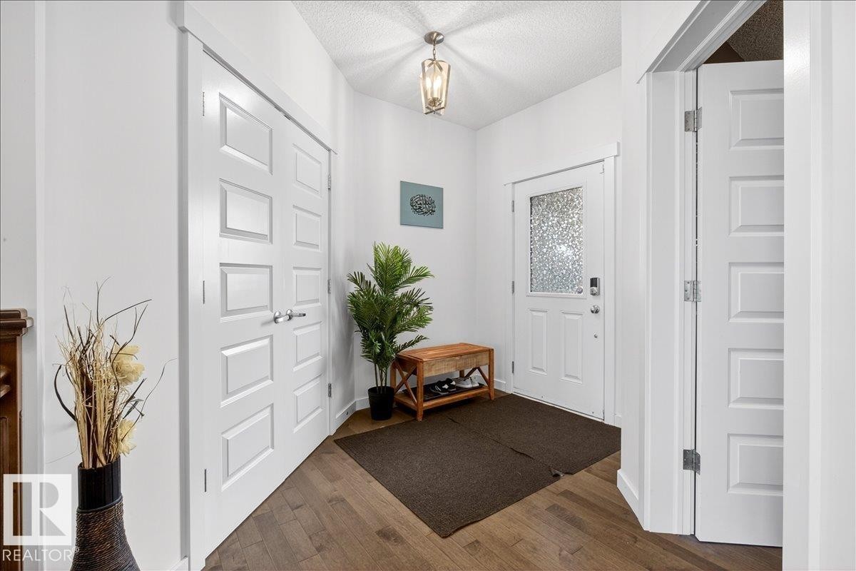 Entryway featuring wood-finish flooring, white paneled doors, and a decorative pendant light - 3936 Claxton Loop Sw, Edmonton, AB - Indoor Photo Showing Other Room