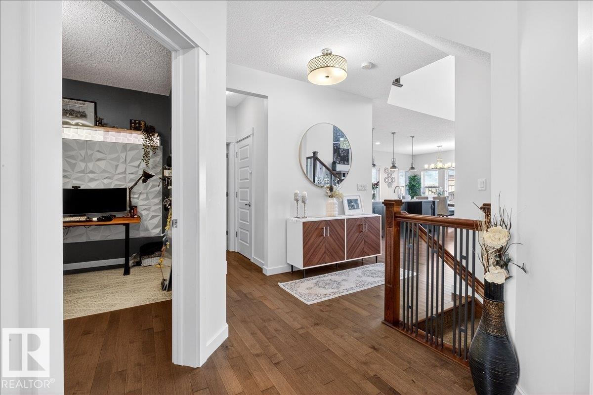 Welcoming foyer showcasing rich wood-finish flooring, white shiplap walls, and a custom wood railing - 3936 Claxton Loop Sw, Edmonton, AB - Indoor Photo Showing Other Room