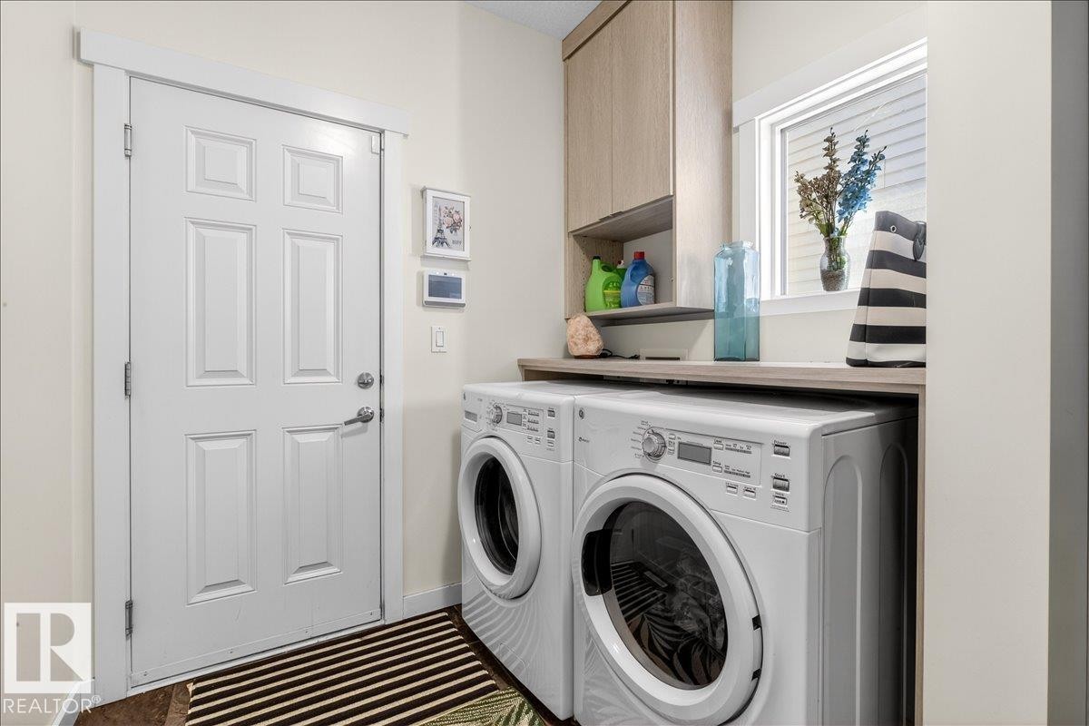 Dedicated laundry room featuring dual front-load washers and dryers with a wood-finish countertop, ample cabinetry storage, and a window for natural light - 3936 Claxton Loop Sw, Edmonton, AB - Indoor Photo Showing Laundry Room
