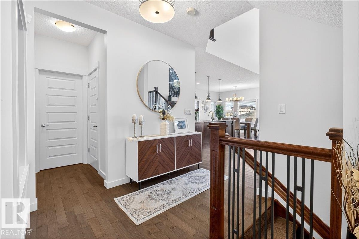 Elegant foyer showcasing rich wood-finish flooring, a custom wood-paneled console with brass hardware, and a circular mirror with brushed metal frame - 3936 Claxton Loop Sw, Edmonton, AB - Indoor Photo Showing Other Room