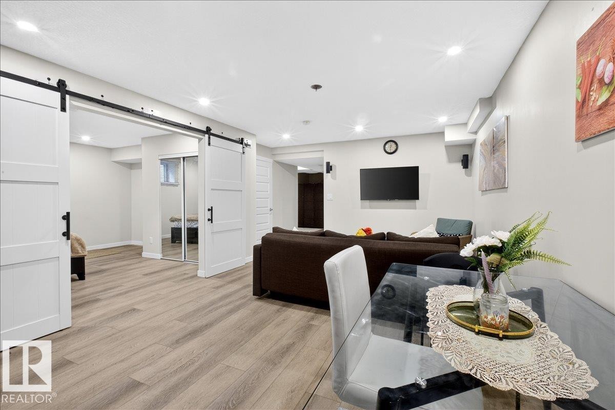 Spacious lower level featuring wood-finish flooring, recessed lighting, and white barn doors with black hardware - 3936 Claxton Loop Sw, Edmonton, AB - Indoor