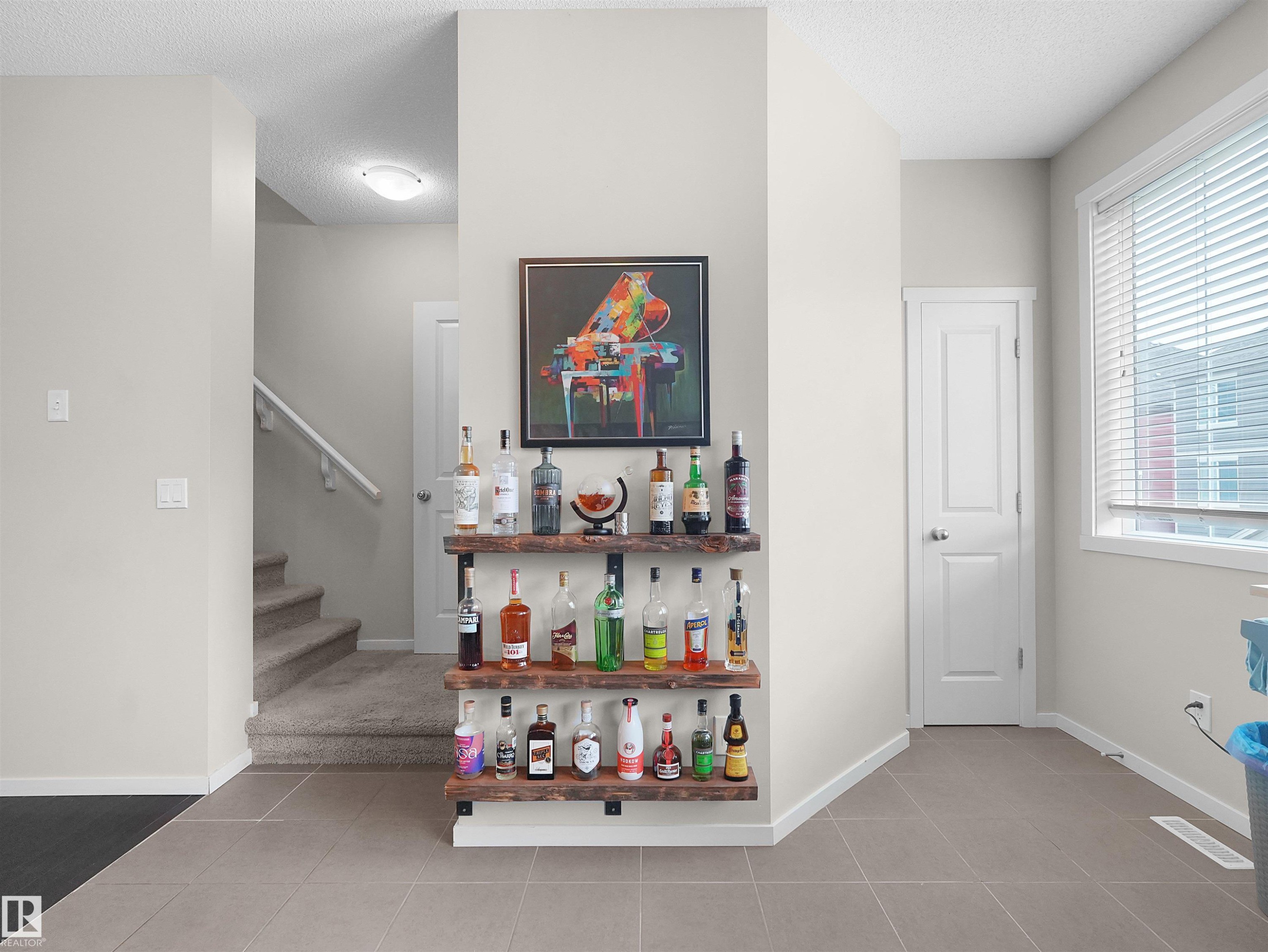 Recessed wall shelving with wood finish, large window with blinds, tile flooring, and carpeted staircase - #89 603 Watt Bv Sw, Edmonton, AB - Indoor Photo Showing Other Room