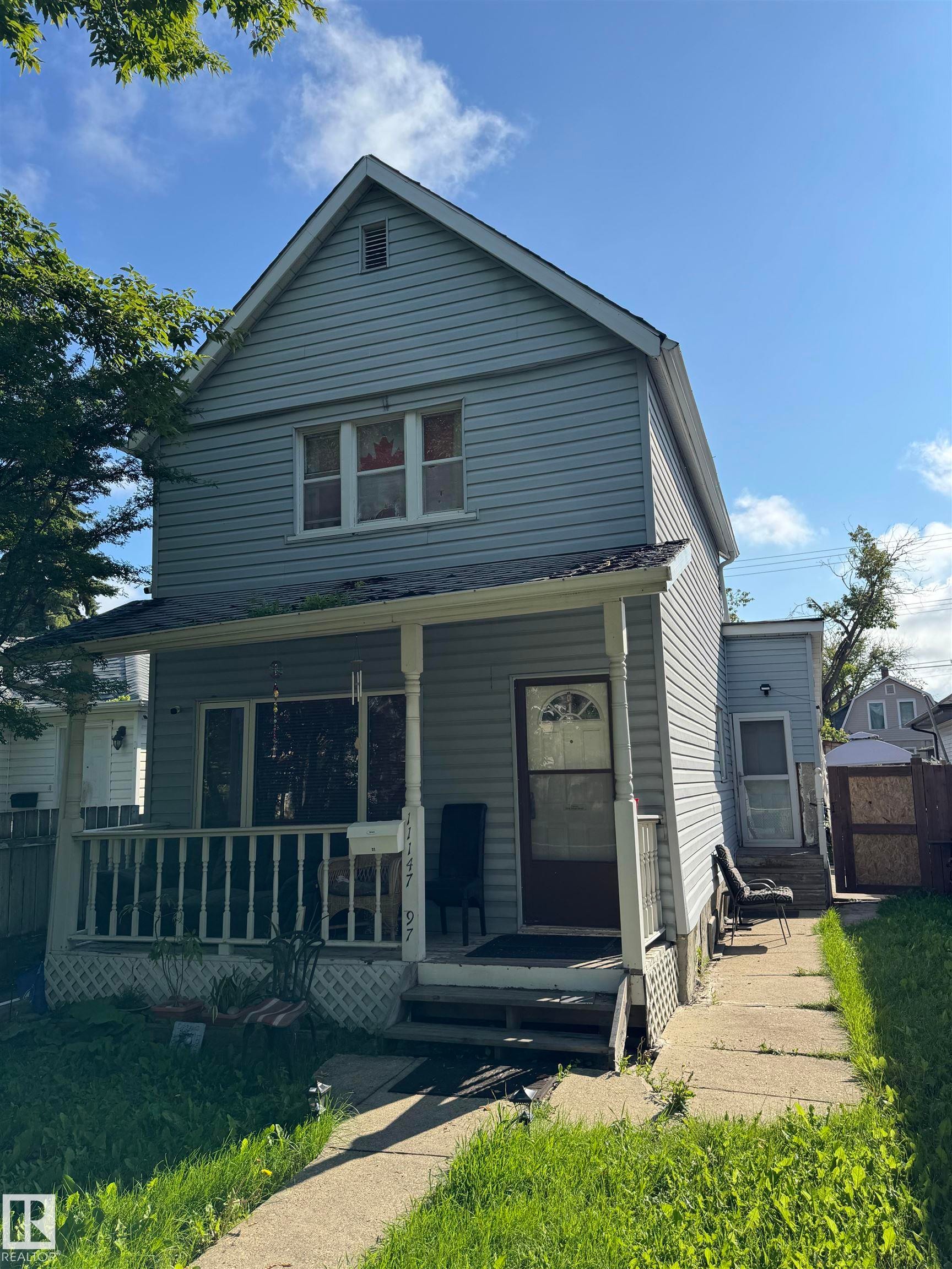 Two-story home featuring horizontal siding exterior, pitched roofline with gable detailing, front-facing covered porch with railings, and multi-pane windows across the facade - 11147 97 Street Nw, Edmonton, AB - Outdoor