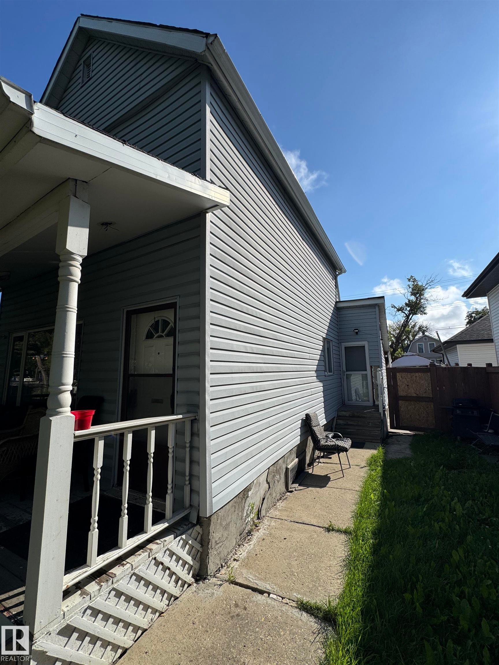 Charming cottage-style home featuring horizontal vinyl siding, a gabled roofline with dark trim, and a covered front porch with white railings and metal steps - 11147 97 Street Nw, Edmonton, AB - Outdoor With Exterior