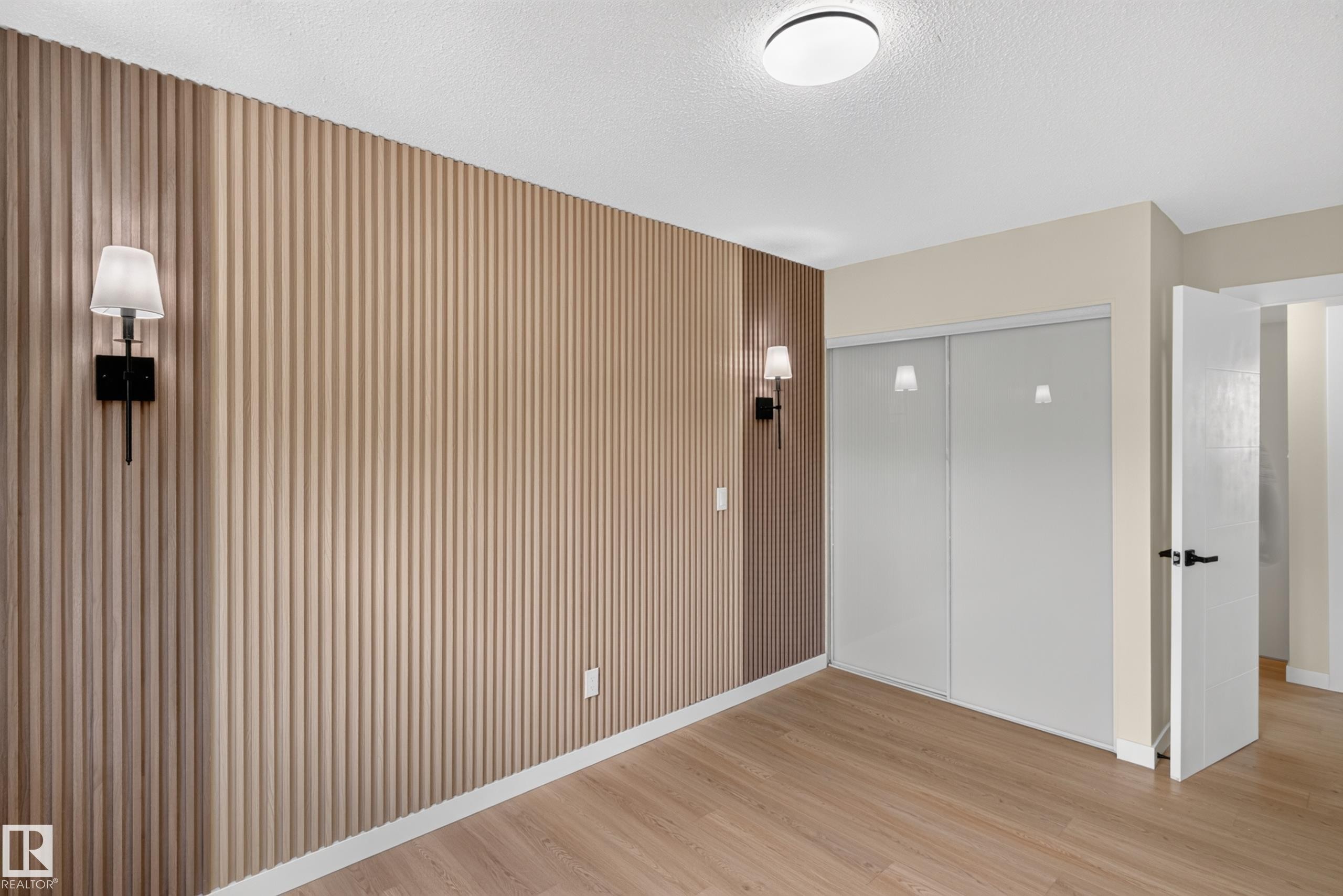 Spacious bedroom featuring warm wood-finish flooring, vertical shiplap accent wall with integrated sconces, and abundant natural light from recessed ceiling fixture - 175 Centennial Crest Nw, Edmonton, AB - Indoor Photo Showing Other Room