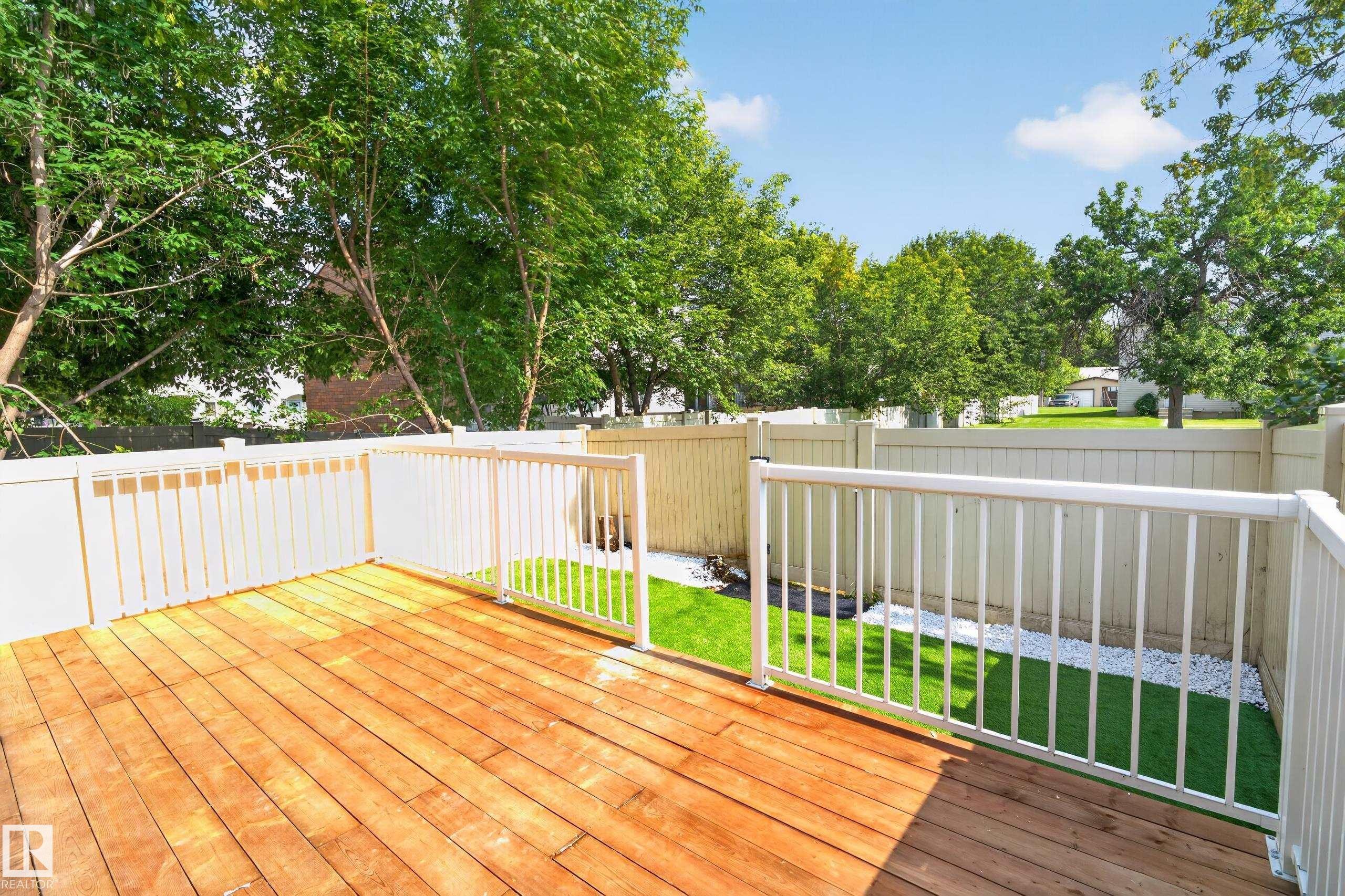 Expansive wood-finish deck with white railings, a fenced perimeter, and a landscaped area featuring artificial turf and white decorative stones - 175 Centennial Crest Nw, Edmonton, AB - Outdoor With Deck Patio Veranda