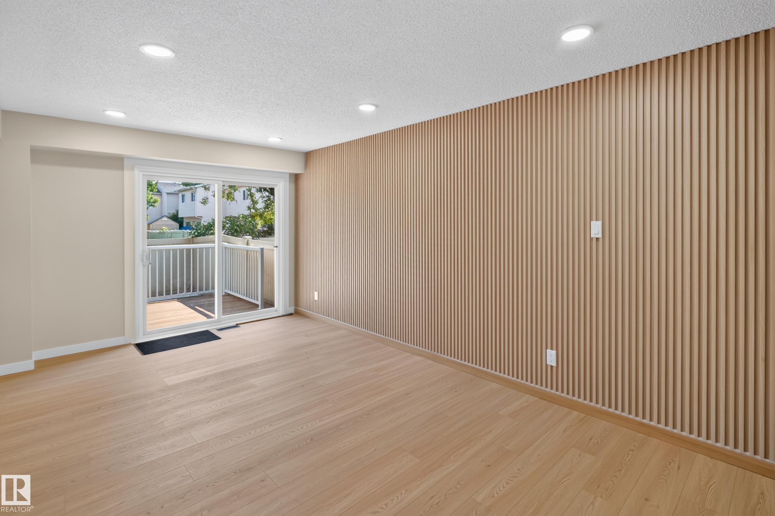 Recessed lighting, wood-finish flooring, accent wall with vertical paneling, sliding glass door, and private balcony - 175 Centennial Crest Nw, Edmonton, AB - Indoor Photo Showing Other Room