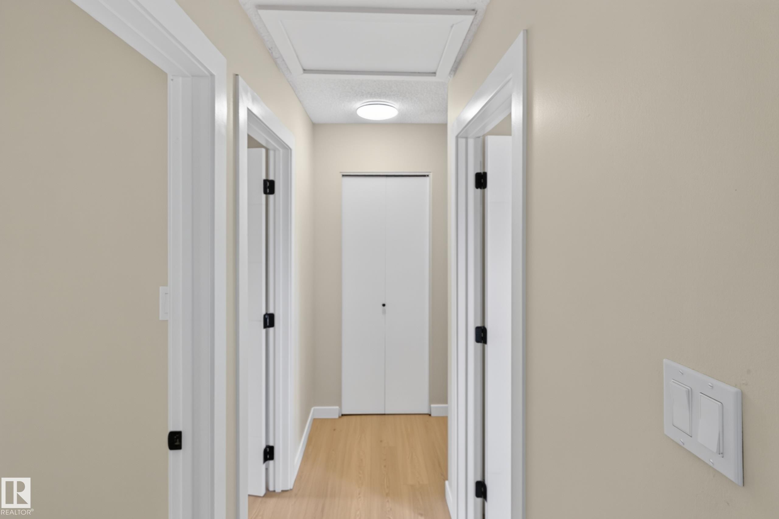Bright hallway with recessed ceiling lighting, wood-finish flooring, and multiple white six-panel doors with black hardware - 175 Centennial Crest Nw, Edmonton, AB - Indoor Photo Showing Other Room