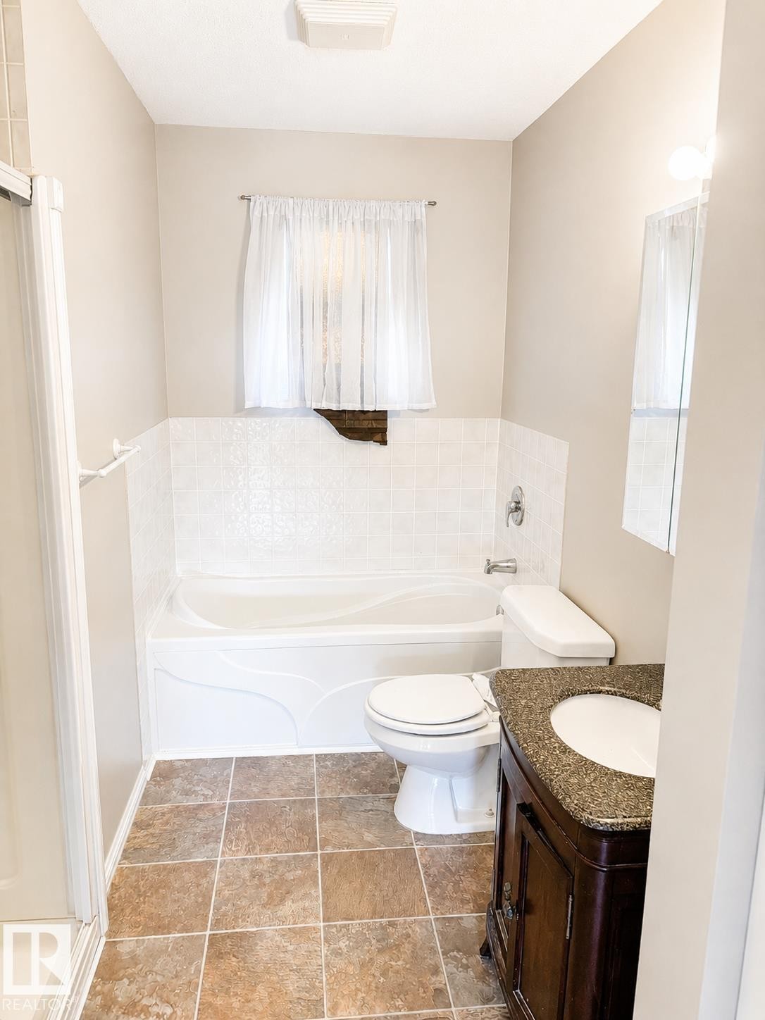 Bathroom featuring a built-in tub with tile surround, a dark wood-finish vanity with a granite-style countertop, and square floor tiling - 802 16 Avenue, Cold Lake, AB - Indoor Photo Showing Bathroom
